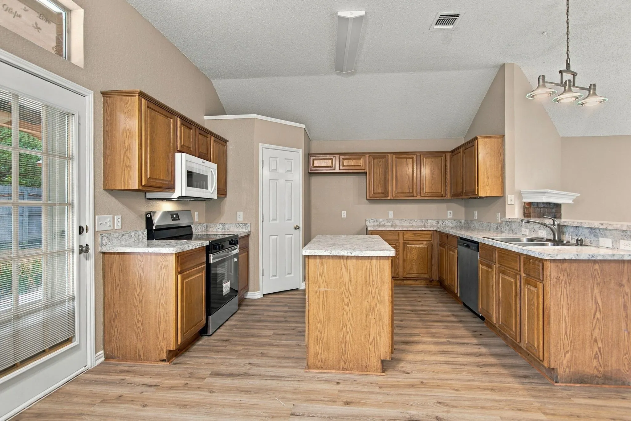Kitchen featuring wood-finish flooring, wood cabinetry, stone-finish countertops, stainless steel appliances, and a central island