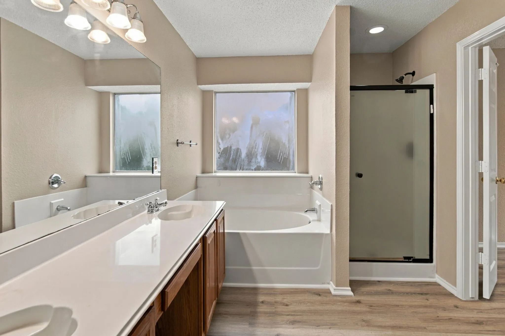 Dual vanity with integrated sinks, built-in soaking tub, glass-enclosed shower, and wood-finish flooring