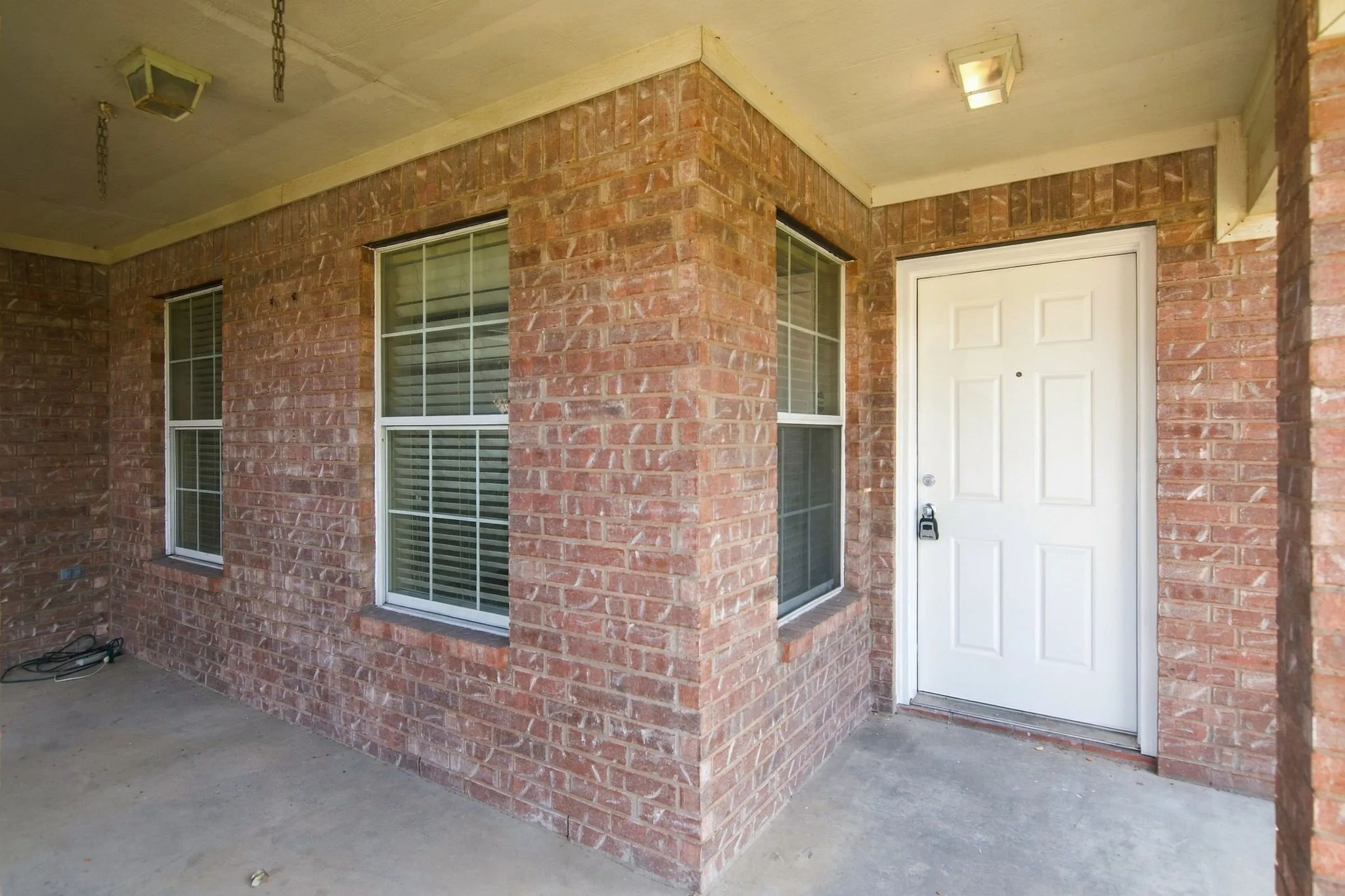Brick exterior with a covered porch, white paneled door, and two double-hung windows