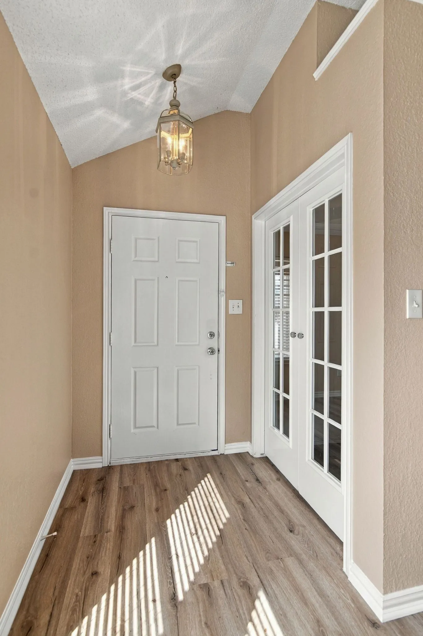 Wood-finish flooring, vaulted ceiling, decorative pendant light fixture, paneled entry door, and French doors