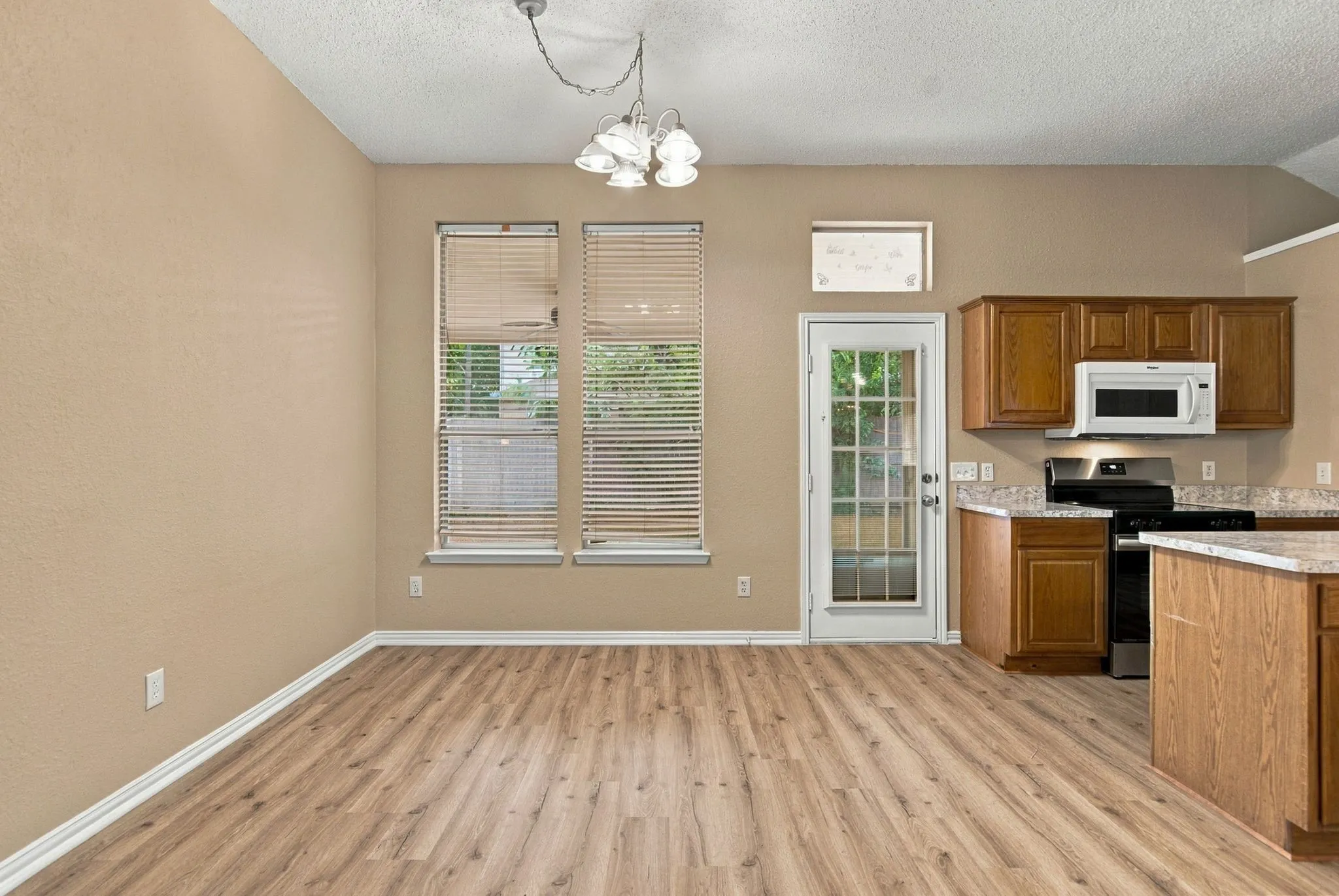 Wood-finish flooring throughout, two large windows, overhead lighting, kitchen with wood cabinetry, and stainless steel stove with microwave above