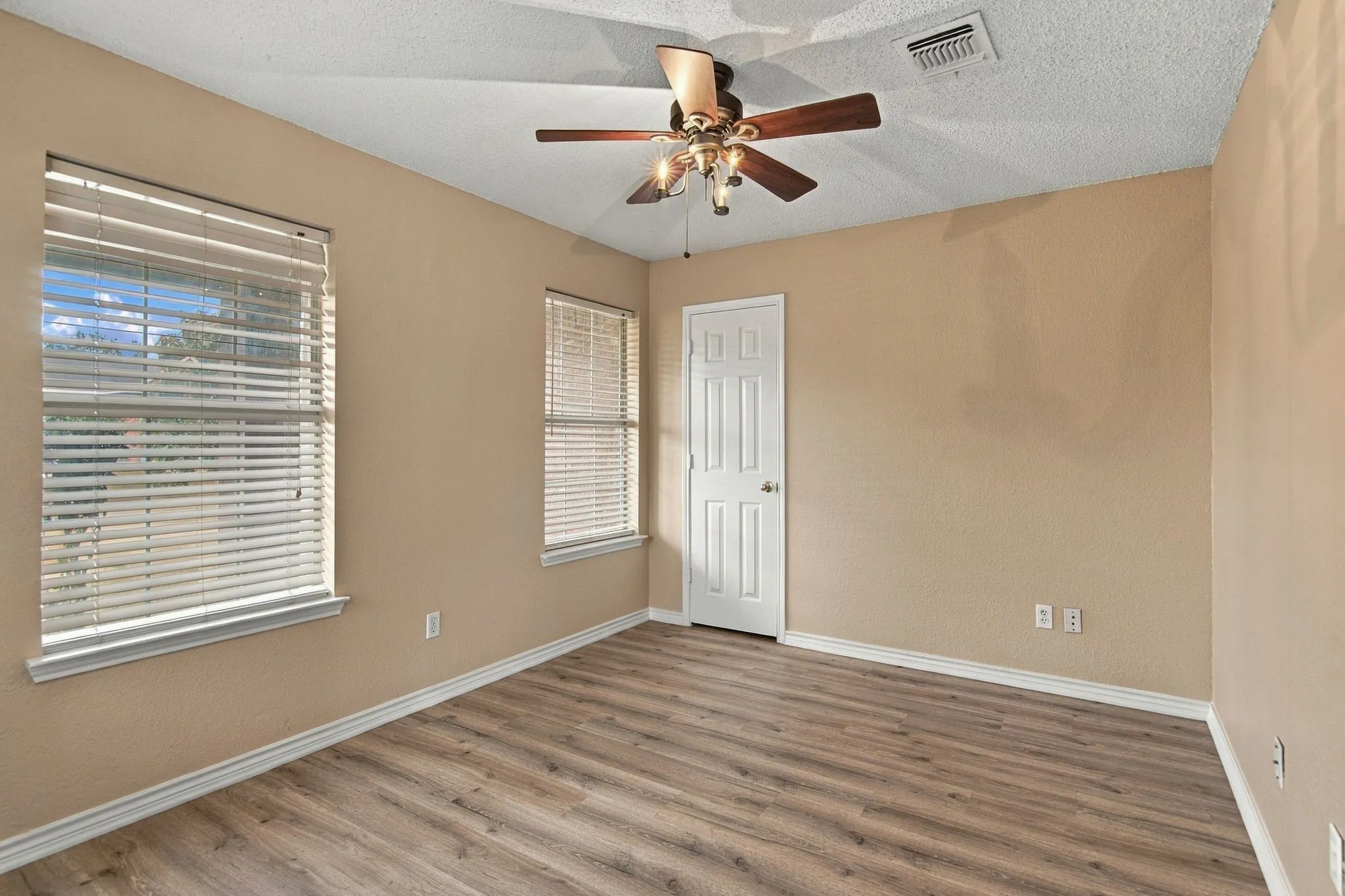 Room featuring two large windows, wood-finish flooring, and a ceiling fan