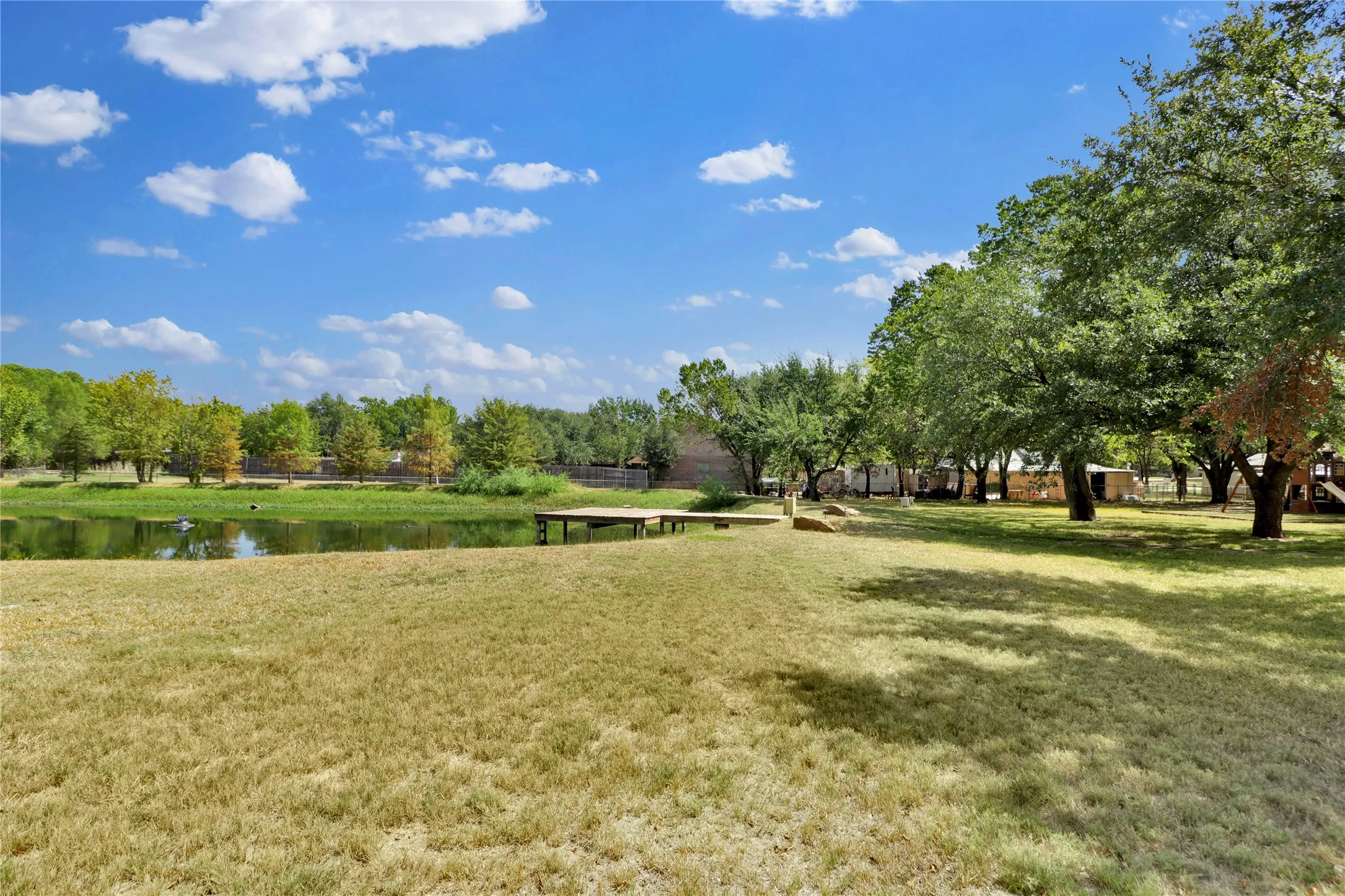 Expansive outdoor space featuring a body of water, a wooden dock, and mature trees