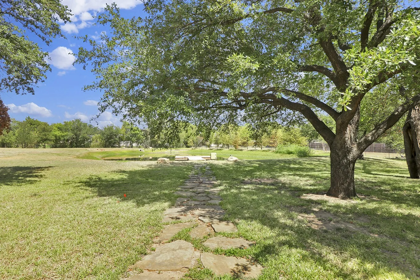 Expansive grassy area featuring mature trees and a stone-paver walkway