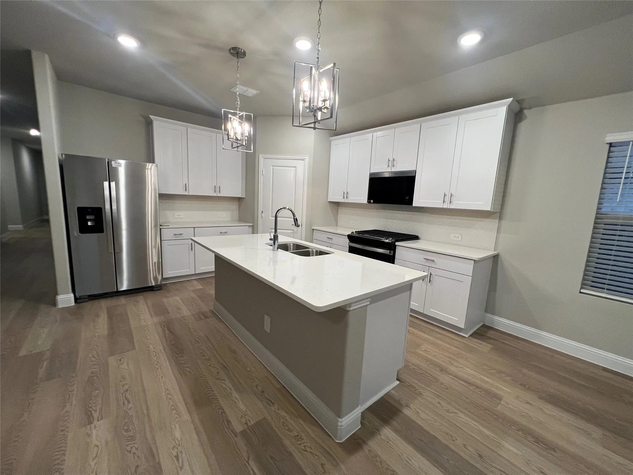 Kitchen featuring a center island, white cabinetry, integrated stainless steel appliances, wood-finish flooring, and recessed lighting