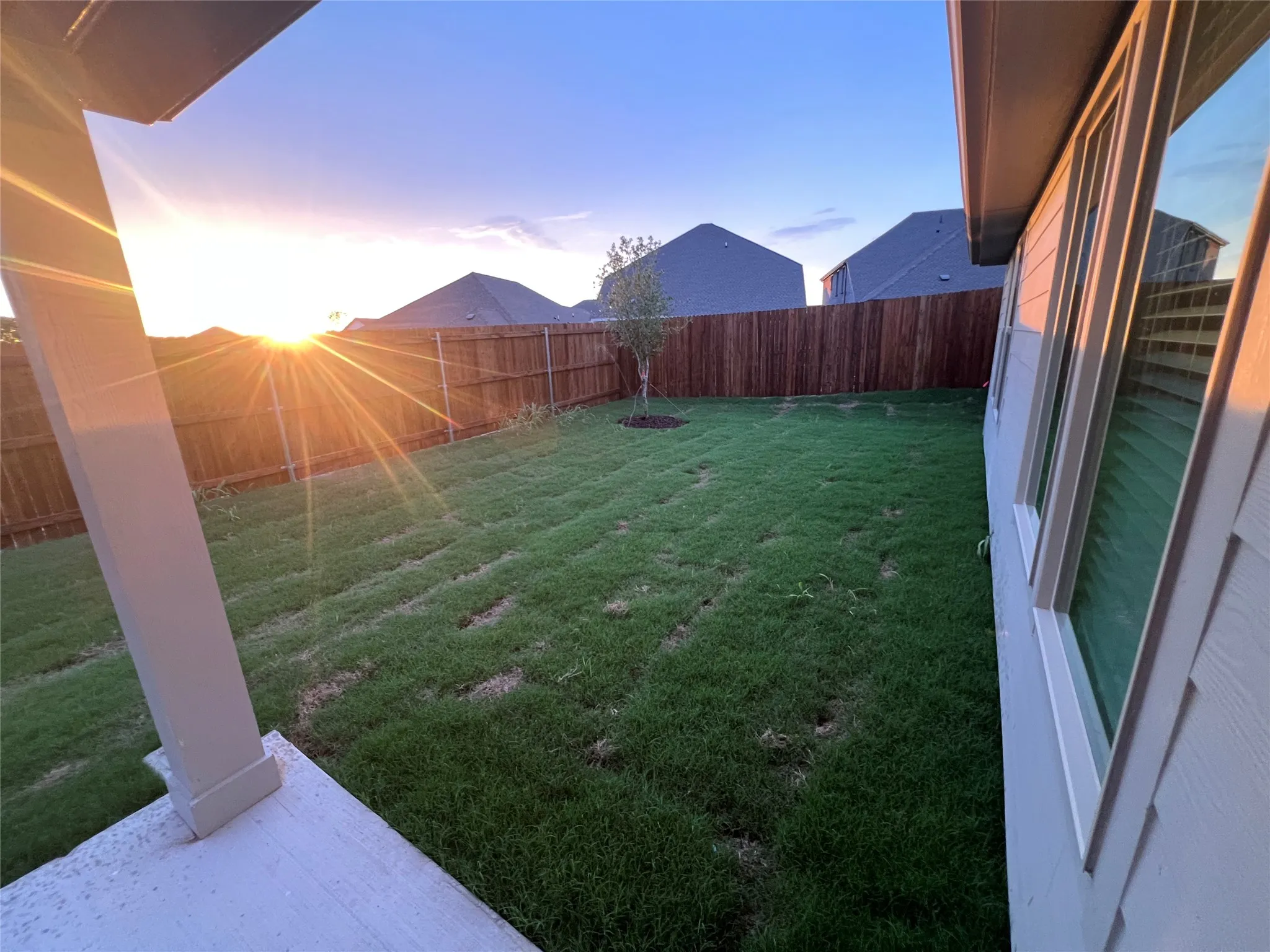Expansive backyard featuring a manicured lawn, full privacy fencing, and a covered patio area