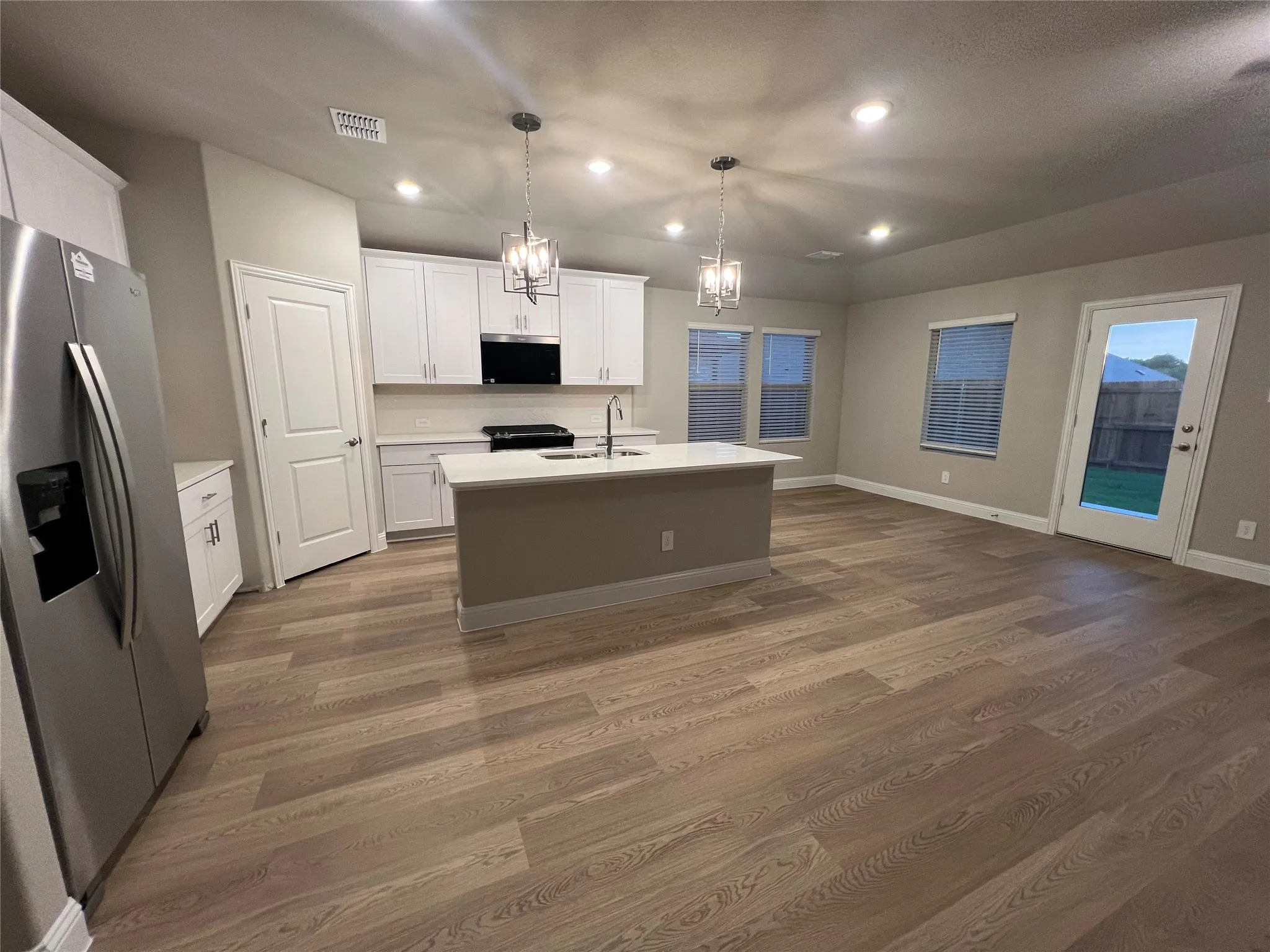 Open-concept kitchen and living area featuring wood-finish flooring, recessed lighting, and a kitchen island with pendant lighting