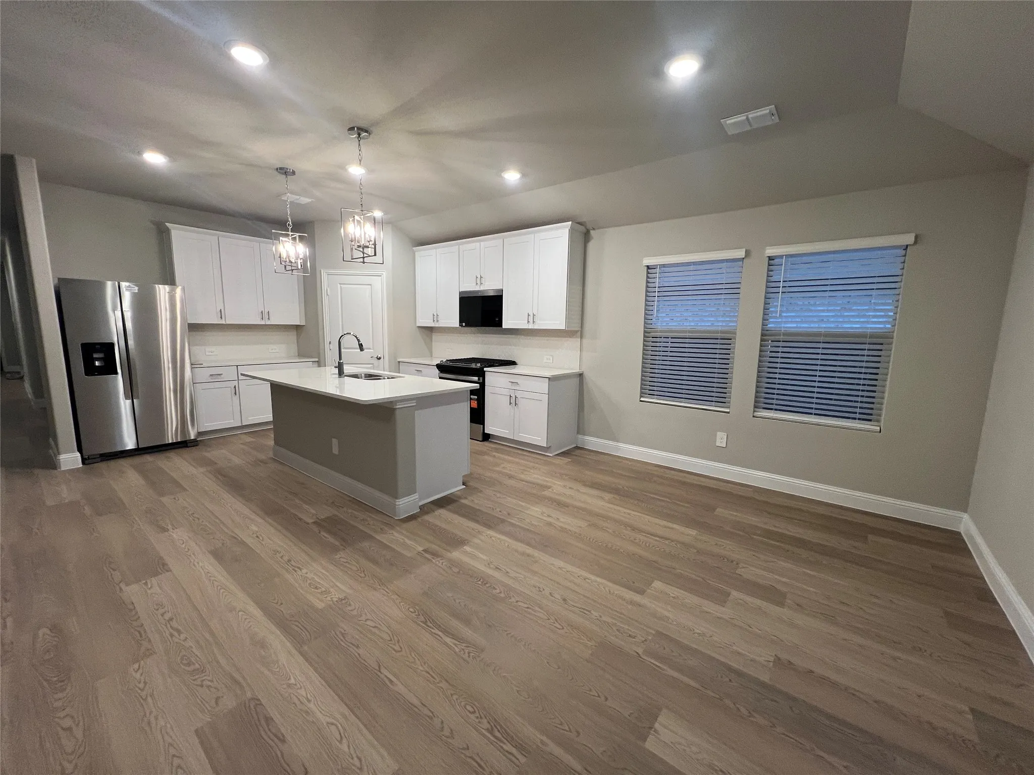 Open-concept kitchen featuring wood-finish flooring, white cabinetry, a central island with a sink, stainless steel appliances, and recessed lighting