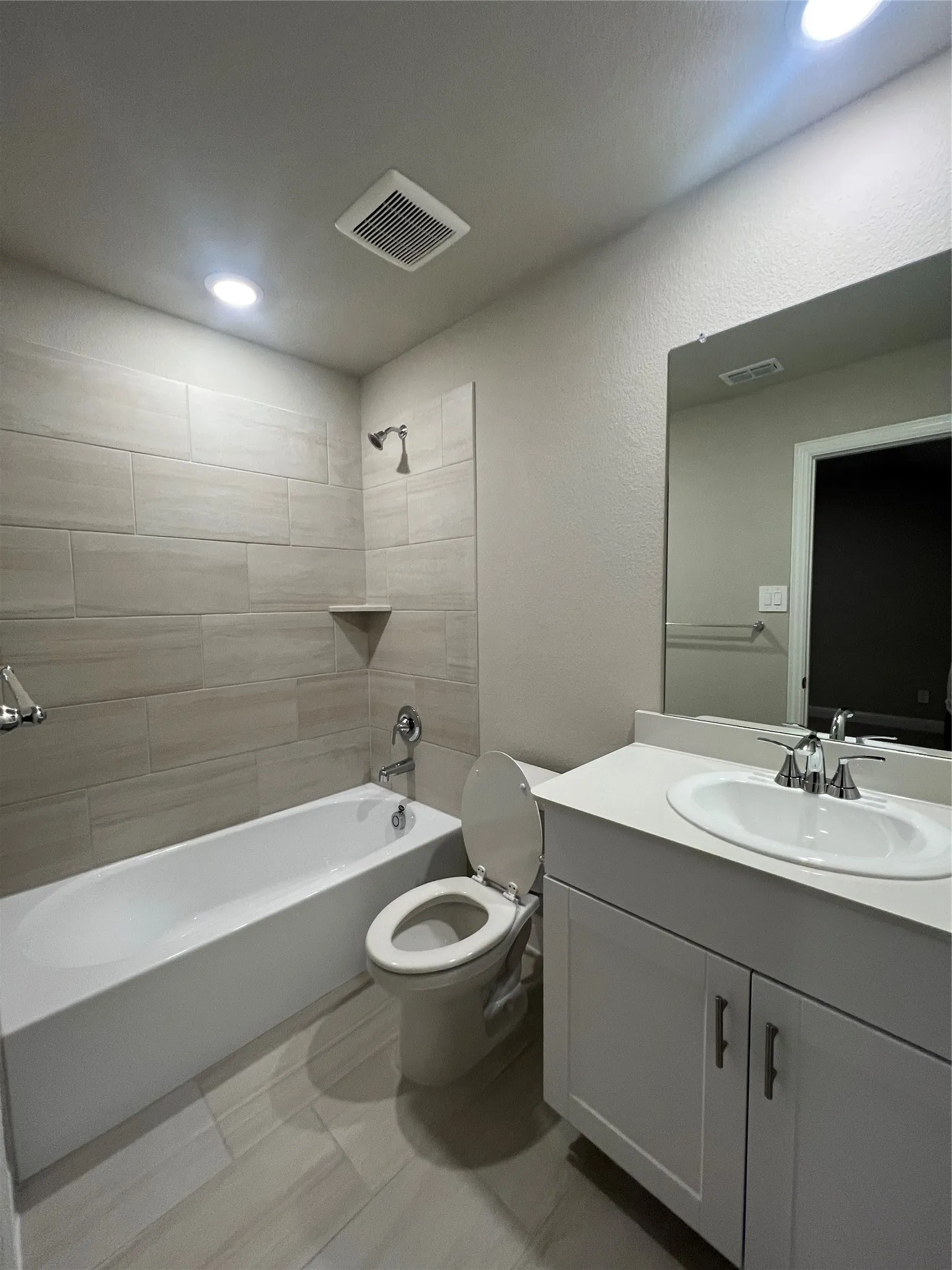 Contemporary bathroom featuring a tub/shower combination with light-toned tiled surround, a built-in shower shelf, a white vanity with shaker-style cabinetry, and a countertop with an integrated sink