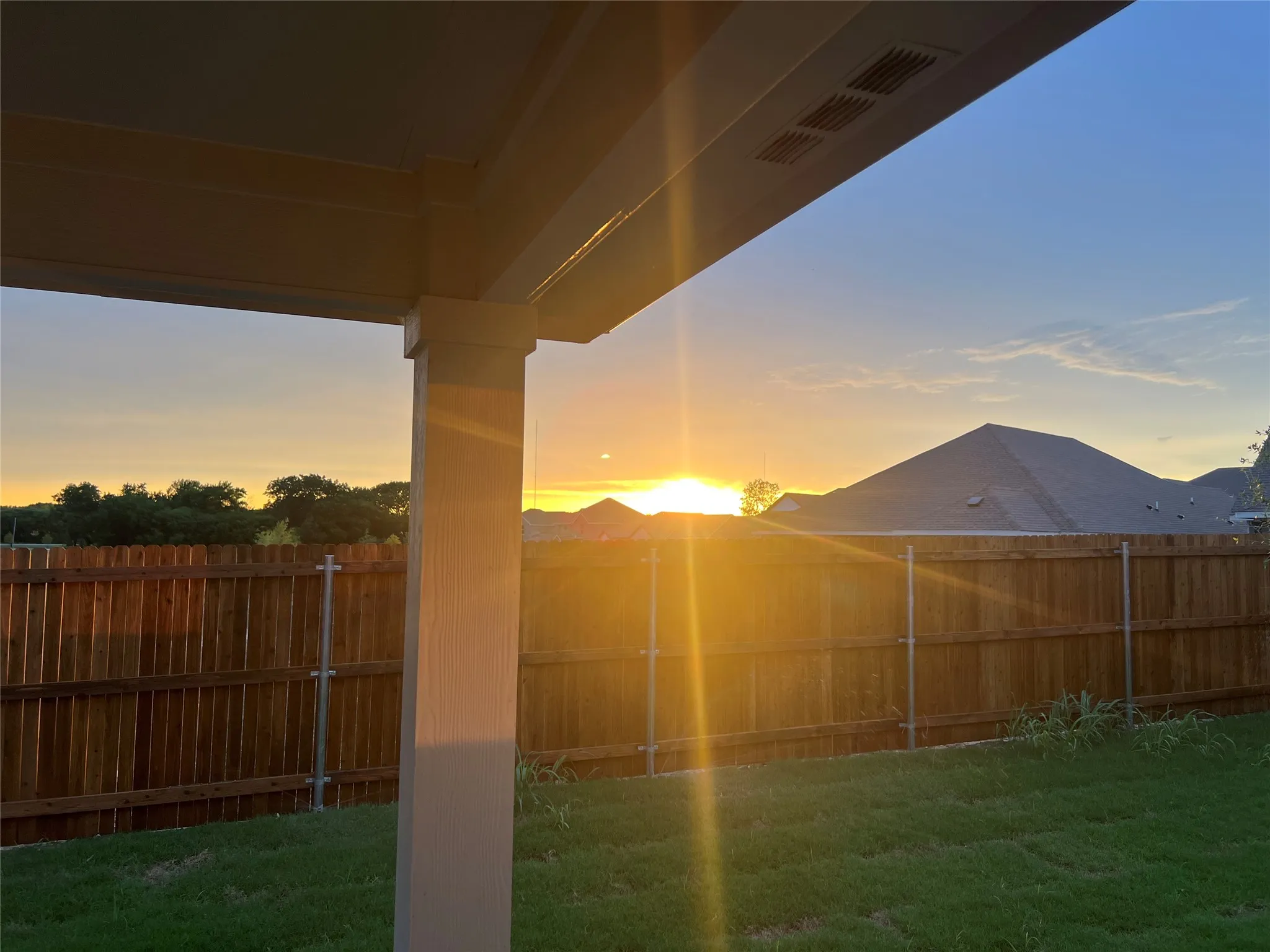 Expansive backyard featuring a manicured lawn, wood privacy fencing, and a covered patio with integrated lighting