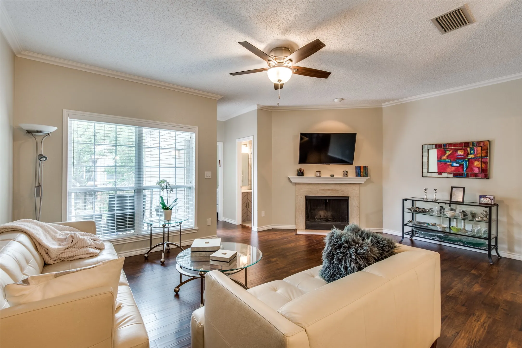 Hardwood-finish flooring, crown molding, ceiling fan with light fixture, and a fireplace with stone surround