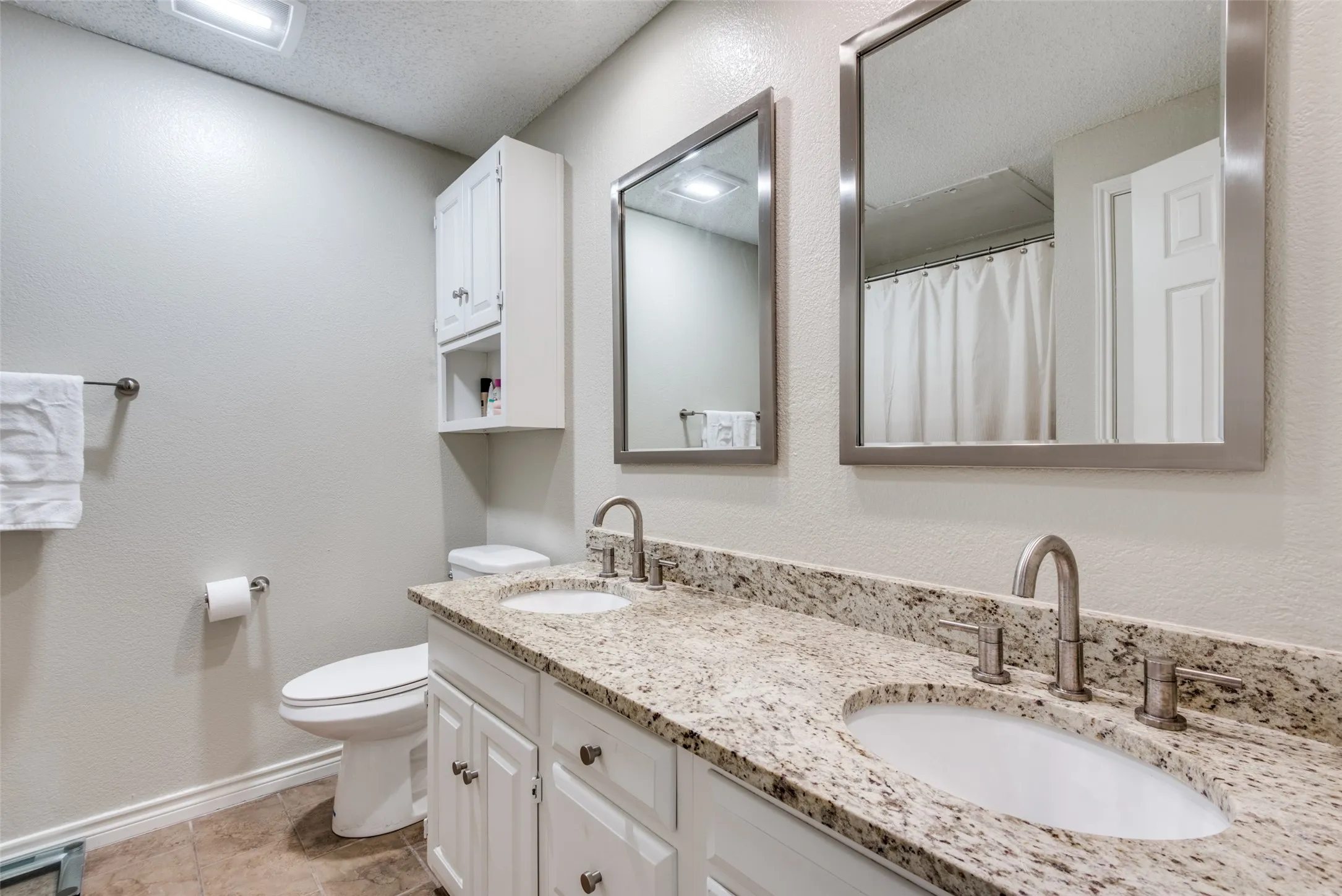 Dual vanity with integrated sinks, granite countertop, brushed nickel fixtures, and white cabinetry