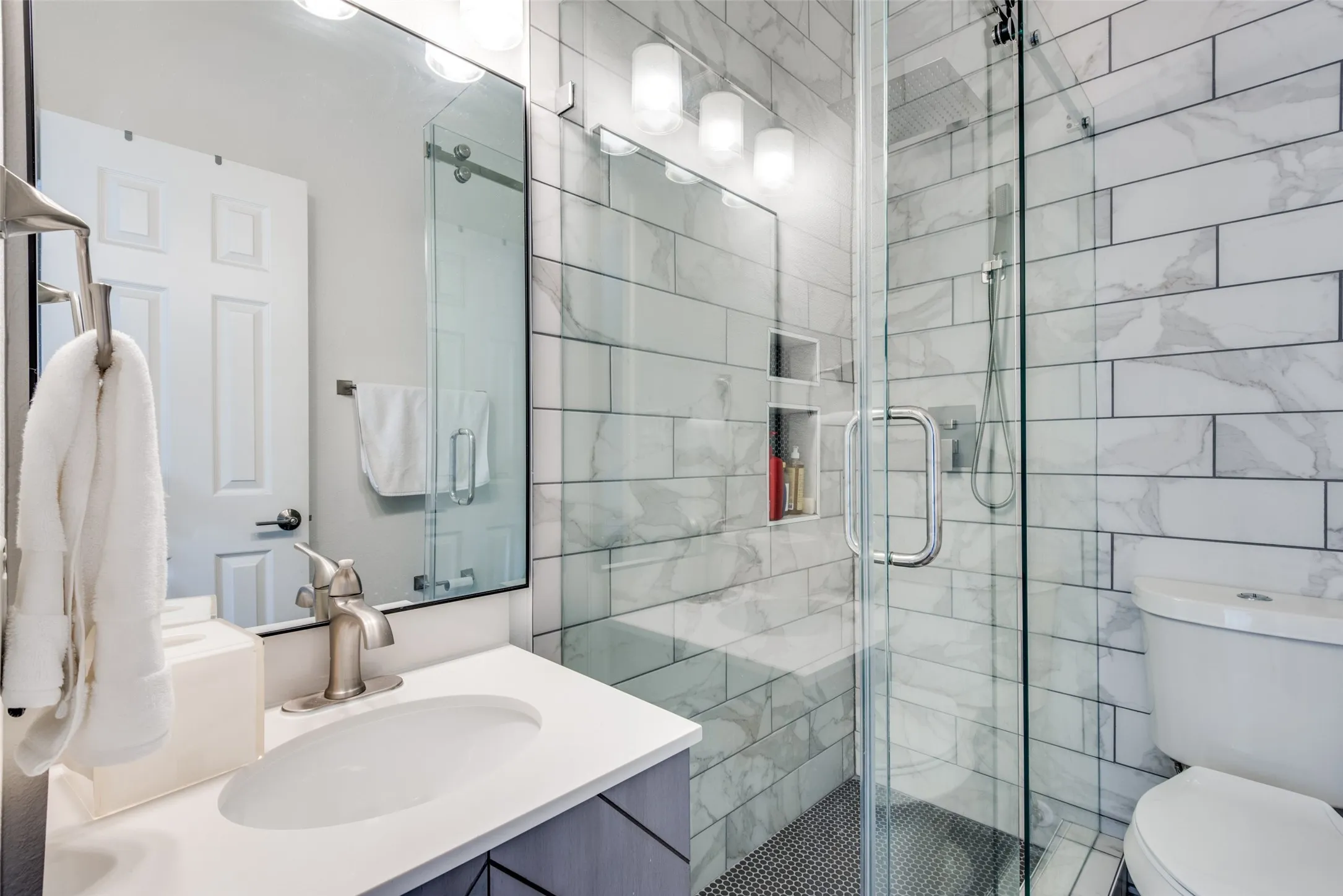 Glass-enclosed shower with subway tile surround, integrated shower niches, a tiled shower bench, and a dark tile shower pan
