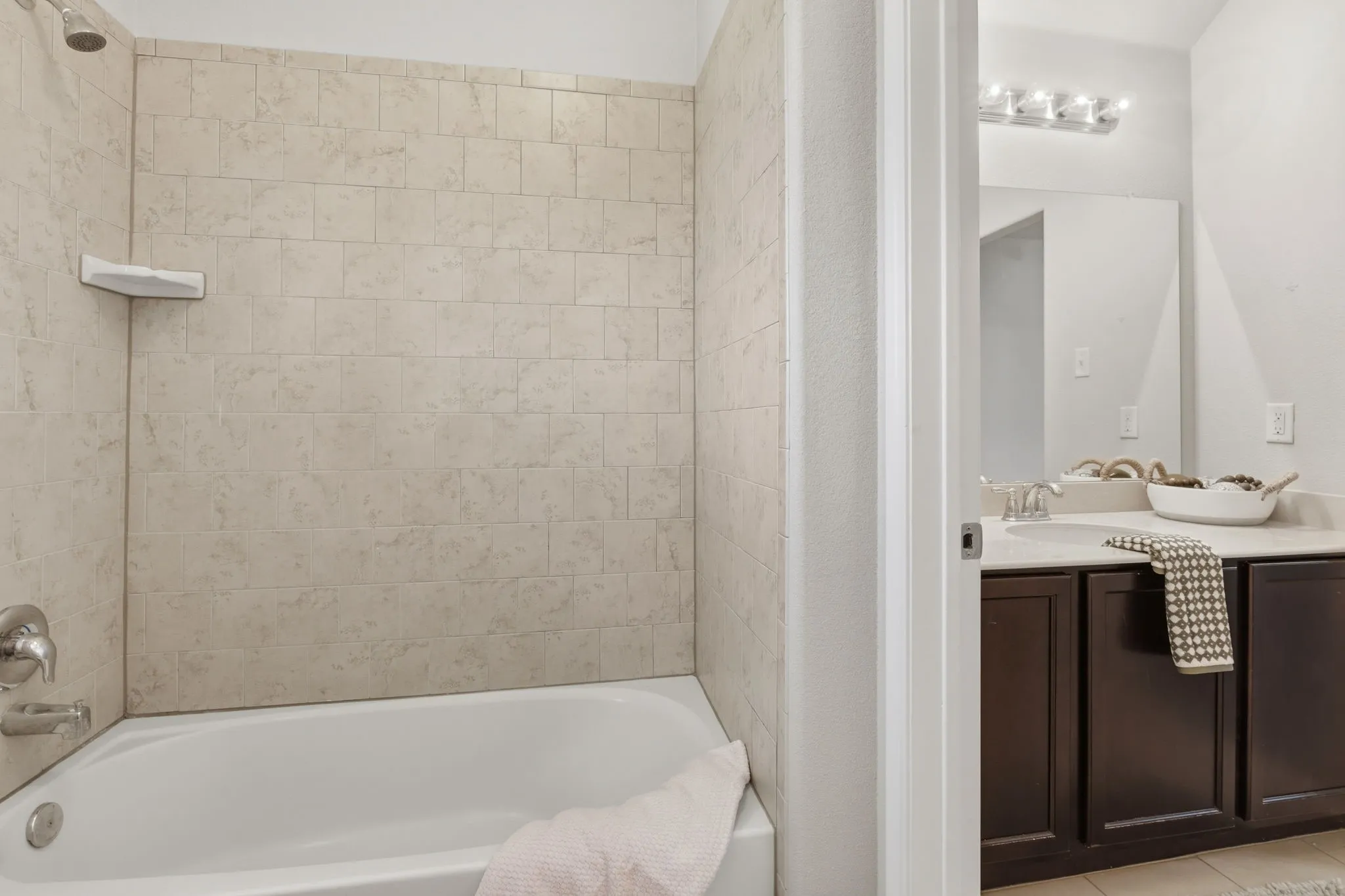 Bathtub with tiled surround, chrome fixtures, and corner shelf