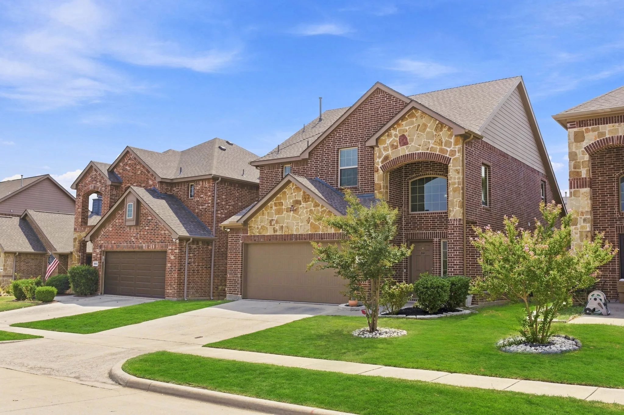 Brick and stone veneer exterior with gabled roofs, multiple windows, attached garages, and landscaped front yards