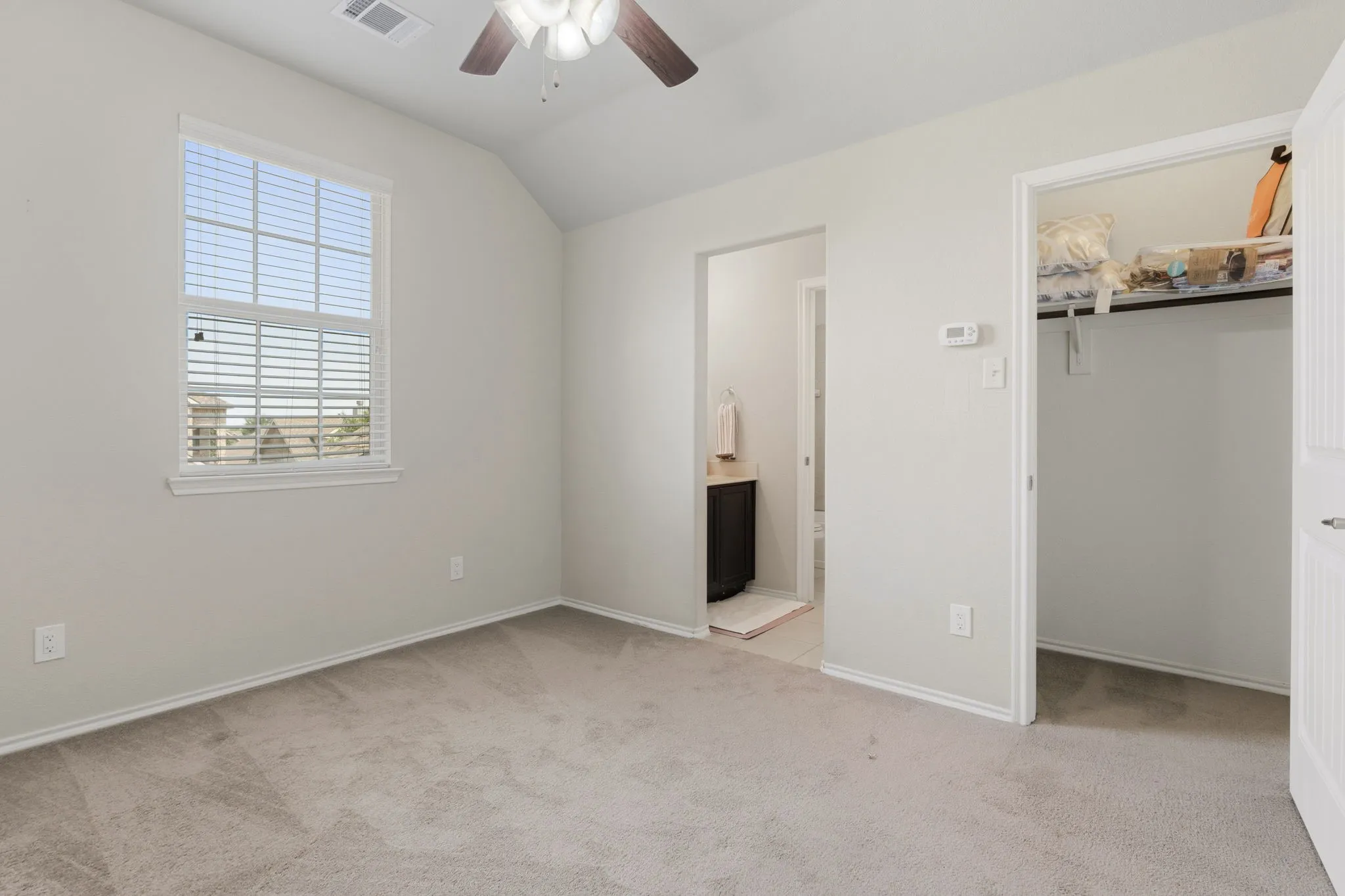 Carpeted room with a vaulted ceiling, ceiling fan, and a window with blinds