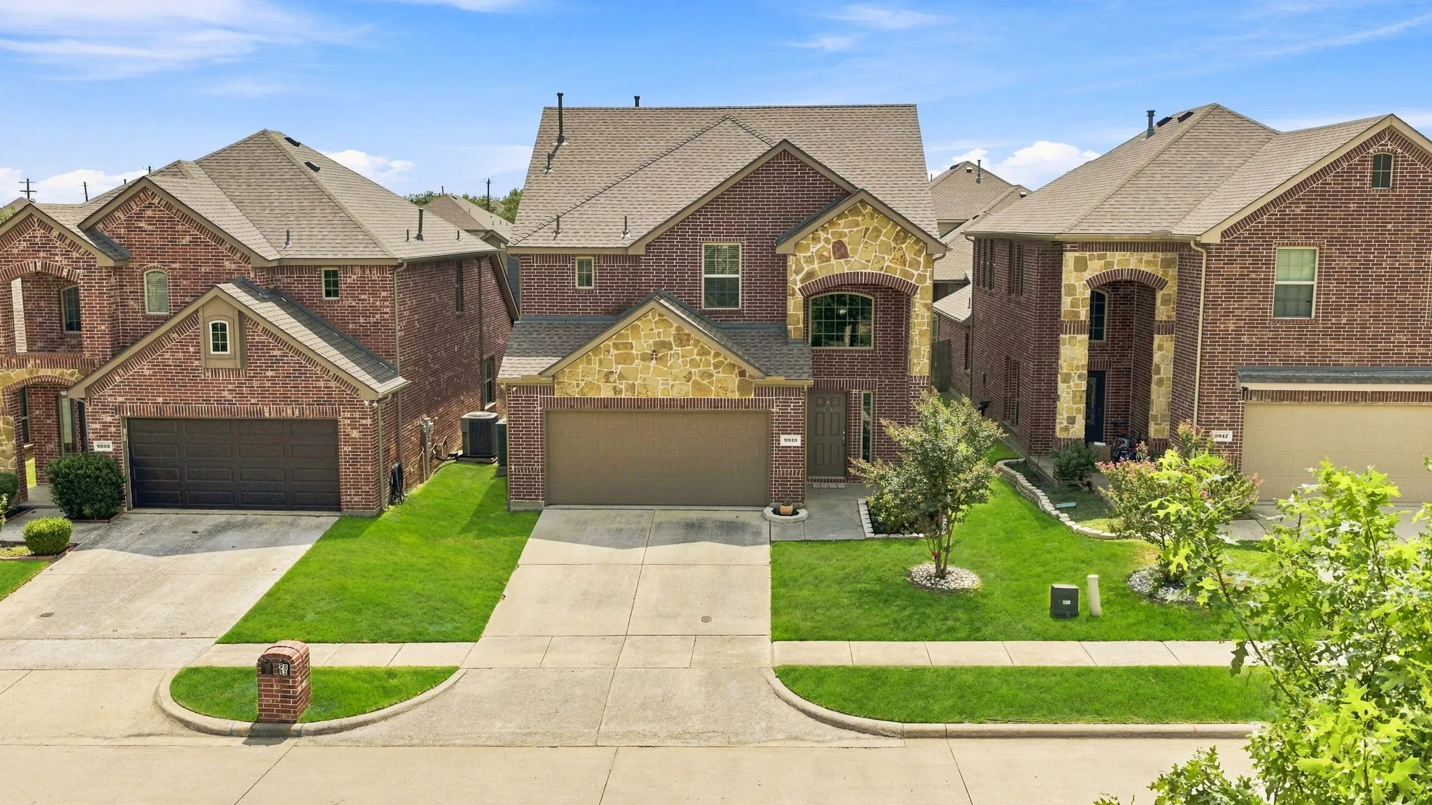Brick facade with stone accents, two-story architectural design, attached two-car garage, concrete driveway, and a gabled roof