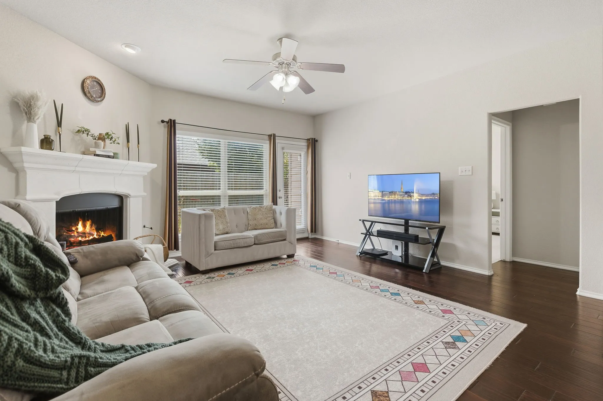 Living area featuring a fireplace with a decorative mantel, wood-finish flooring, and a ceiling fan with integrated lighting