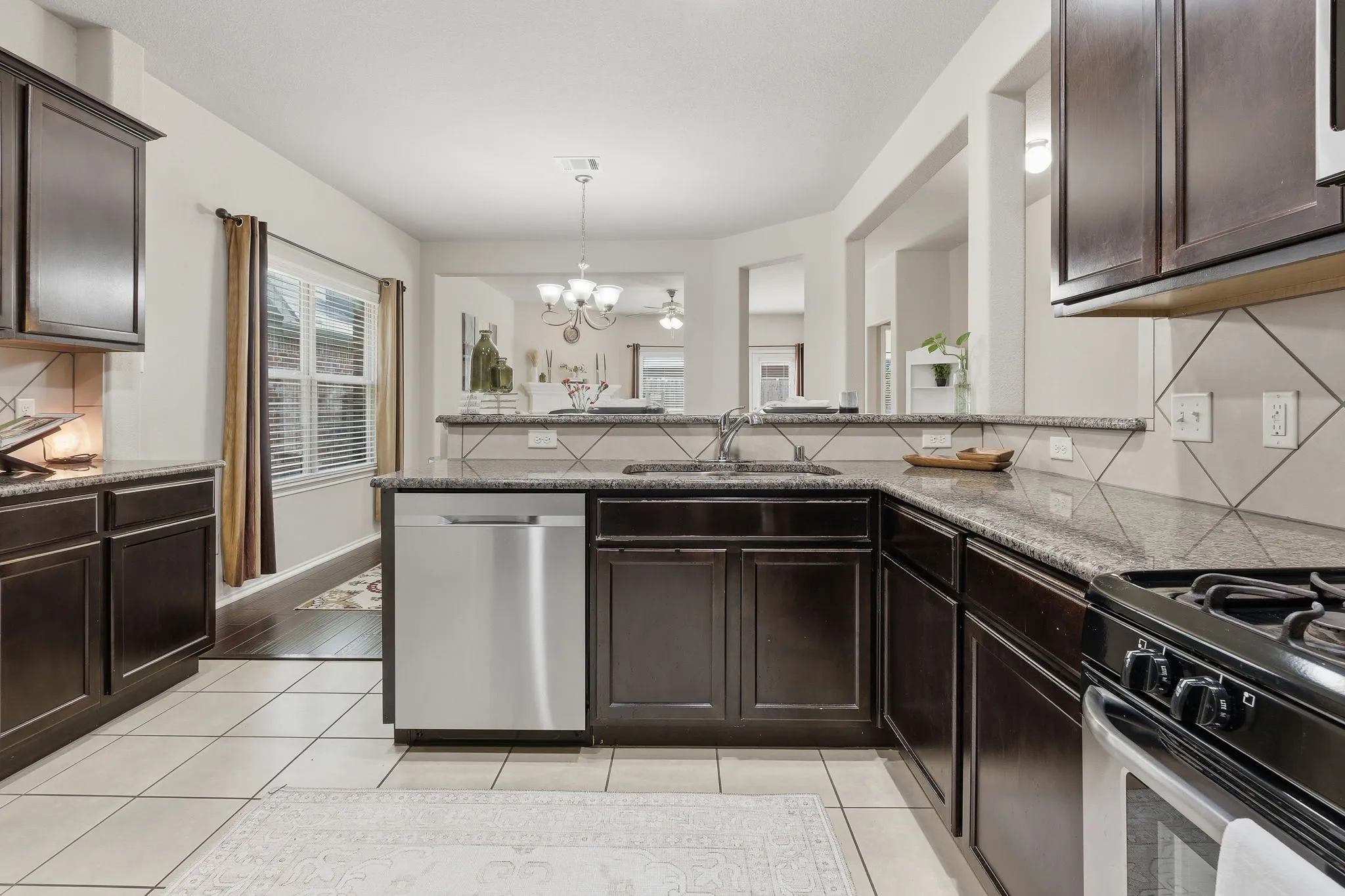 Kitchen featuring dark wood cabinetry, granite countertops, stainless steel dishwasher, tile flooring, and a tile backsplash with a diagonal pattern