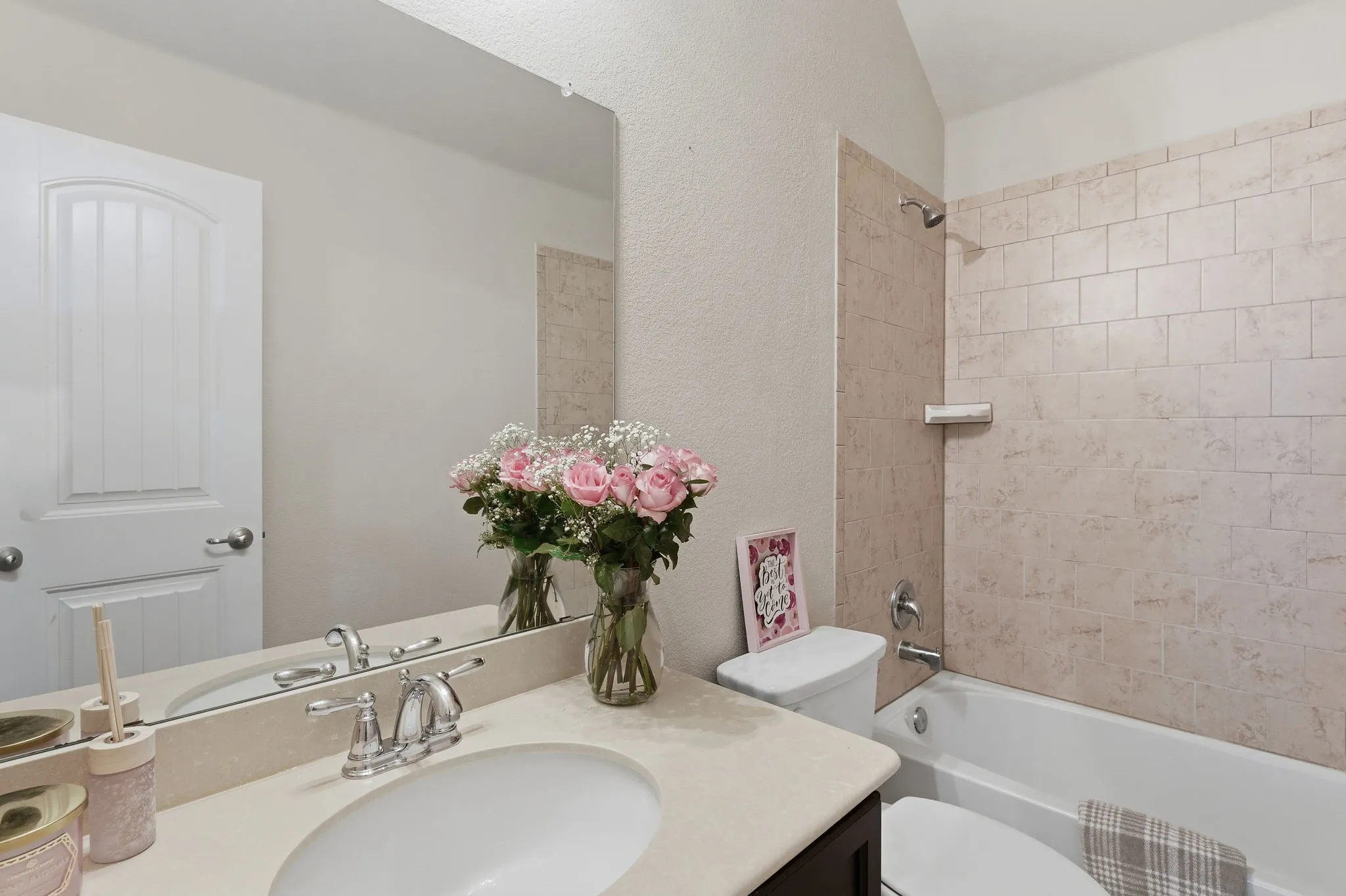 White bathtub with tiled shower surround, single vanity with integrated sink, and wall-mounted mirror