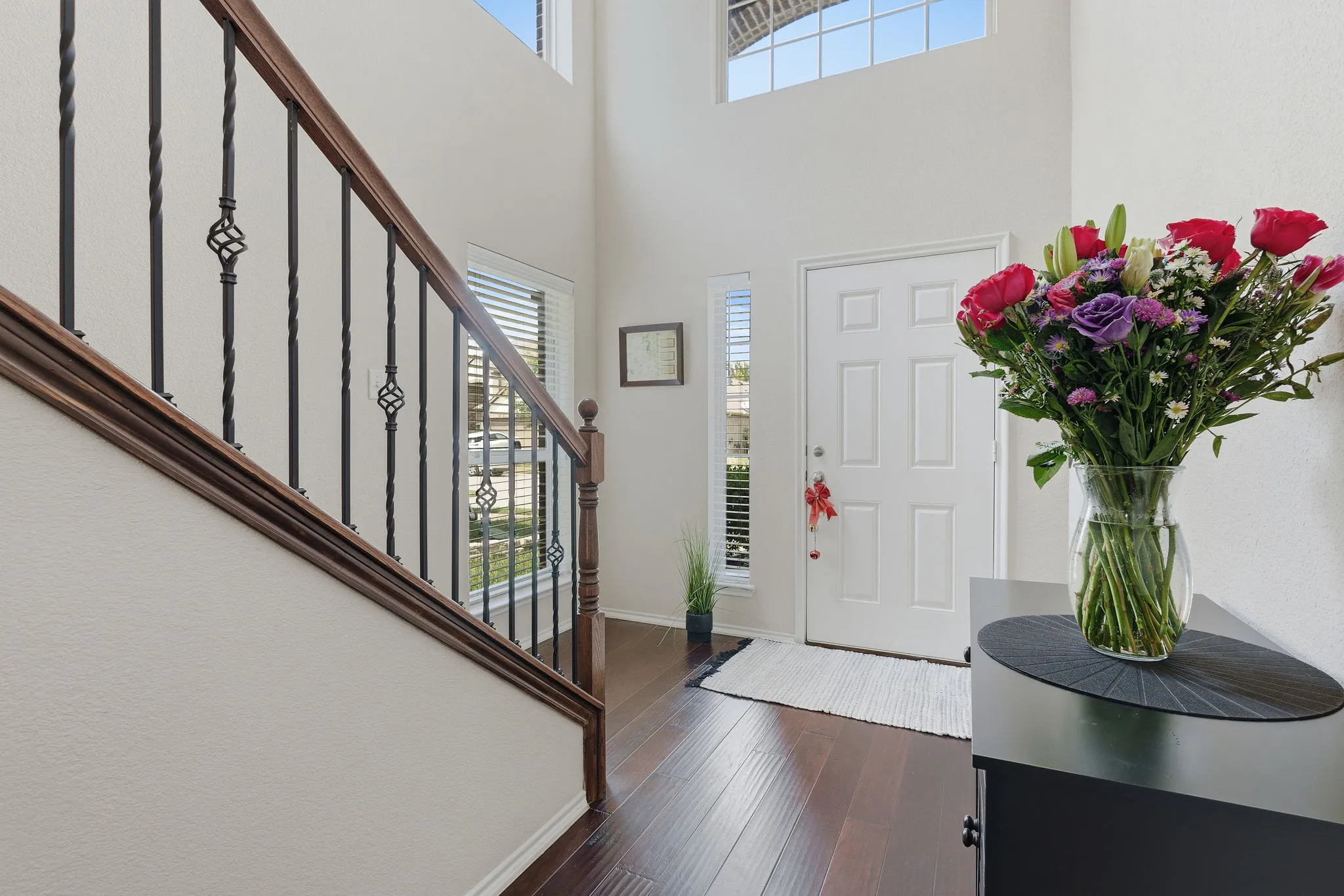 Two-story foyer with high ceilings, dark wood-finish flooring, and a staircase featuring wrought iron balusters with decorative elements