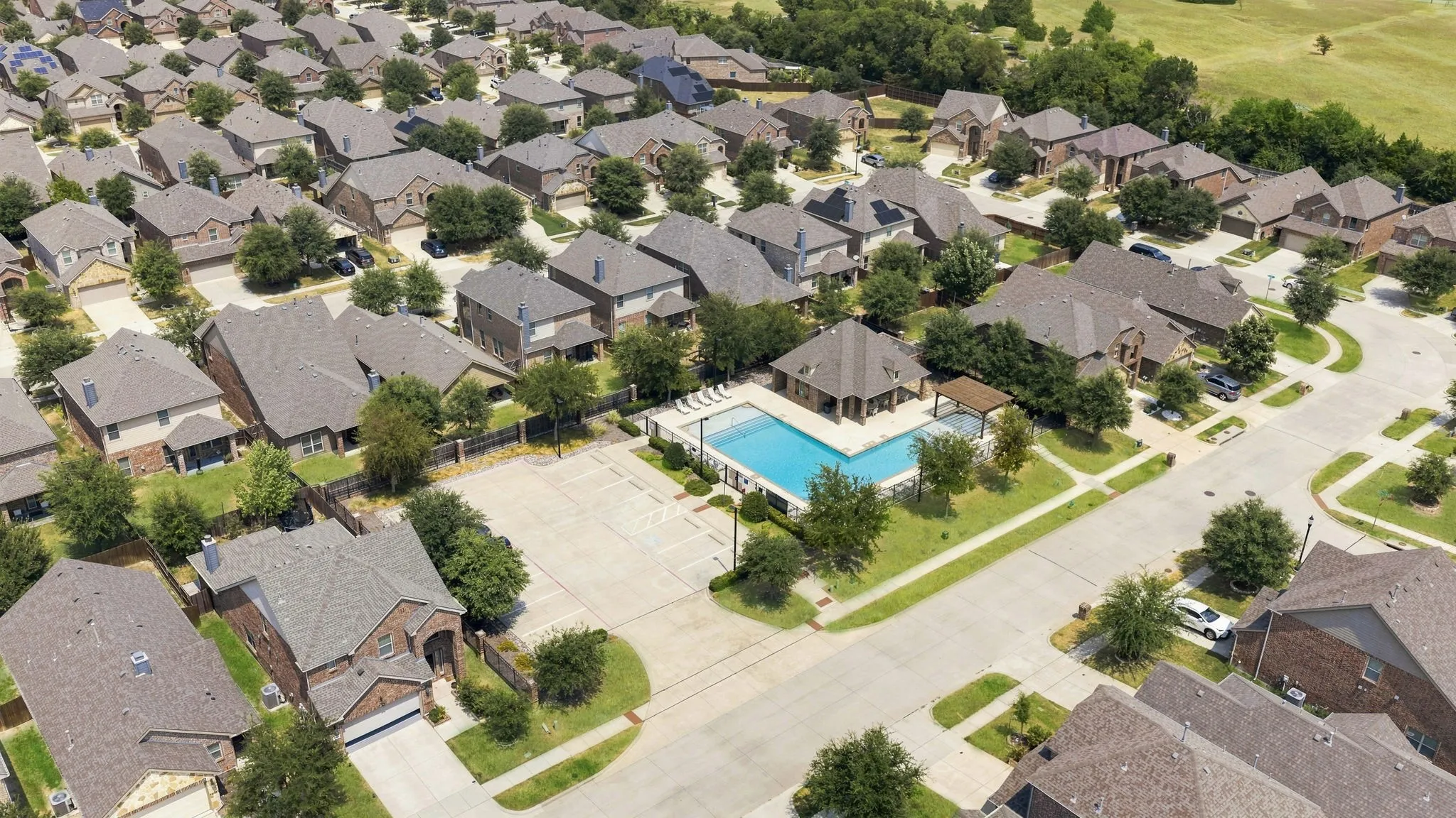 Community pool with surrounding patio, a pergola, and mature trees within a residential development