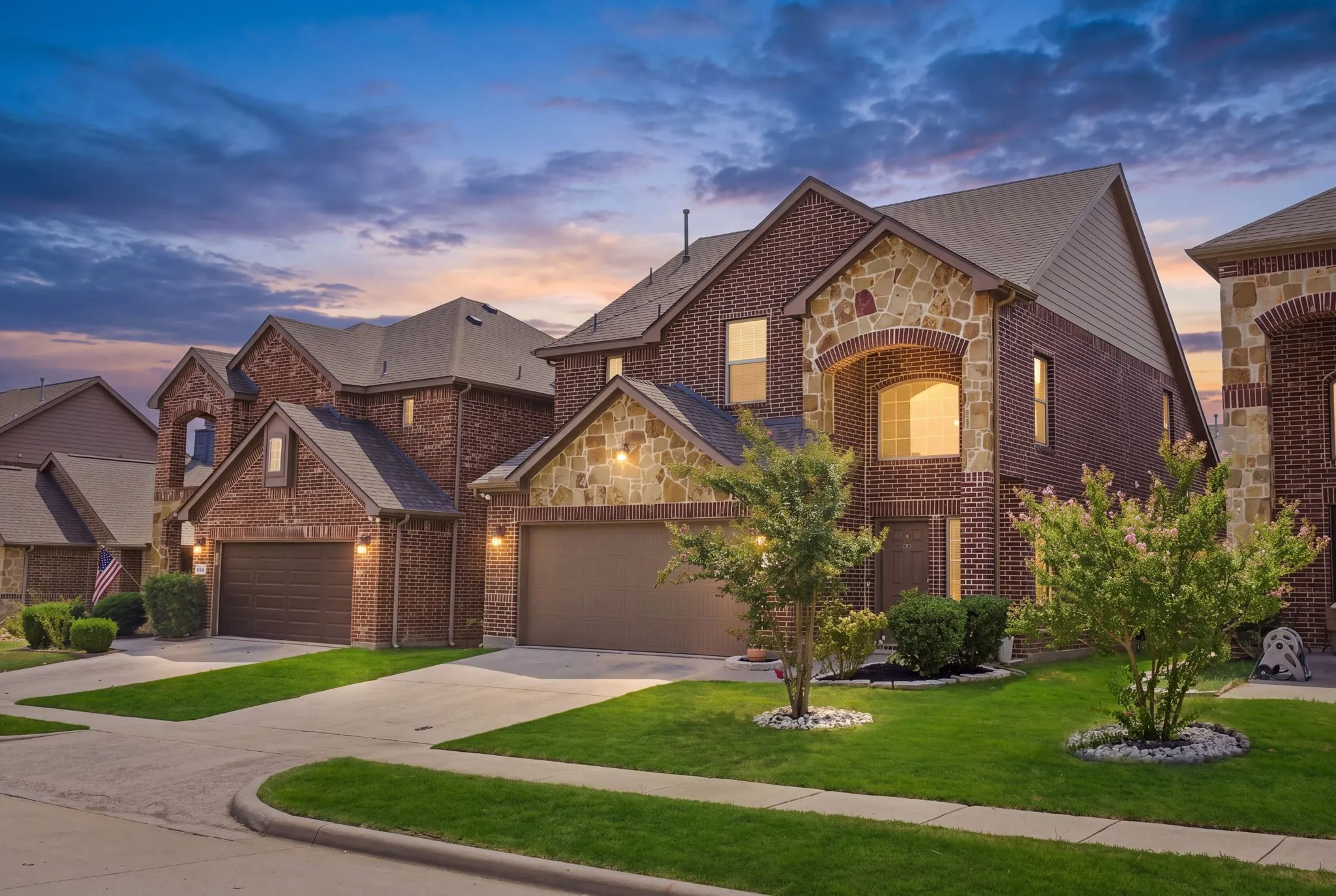 Brick and stone exterior with arched window, integrated two-car garage, and mature landscaping