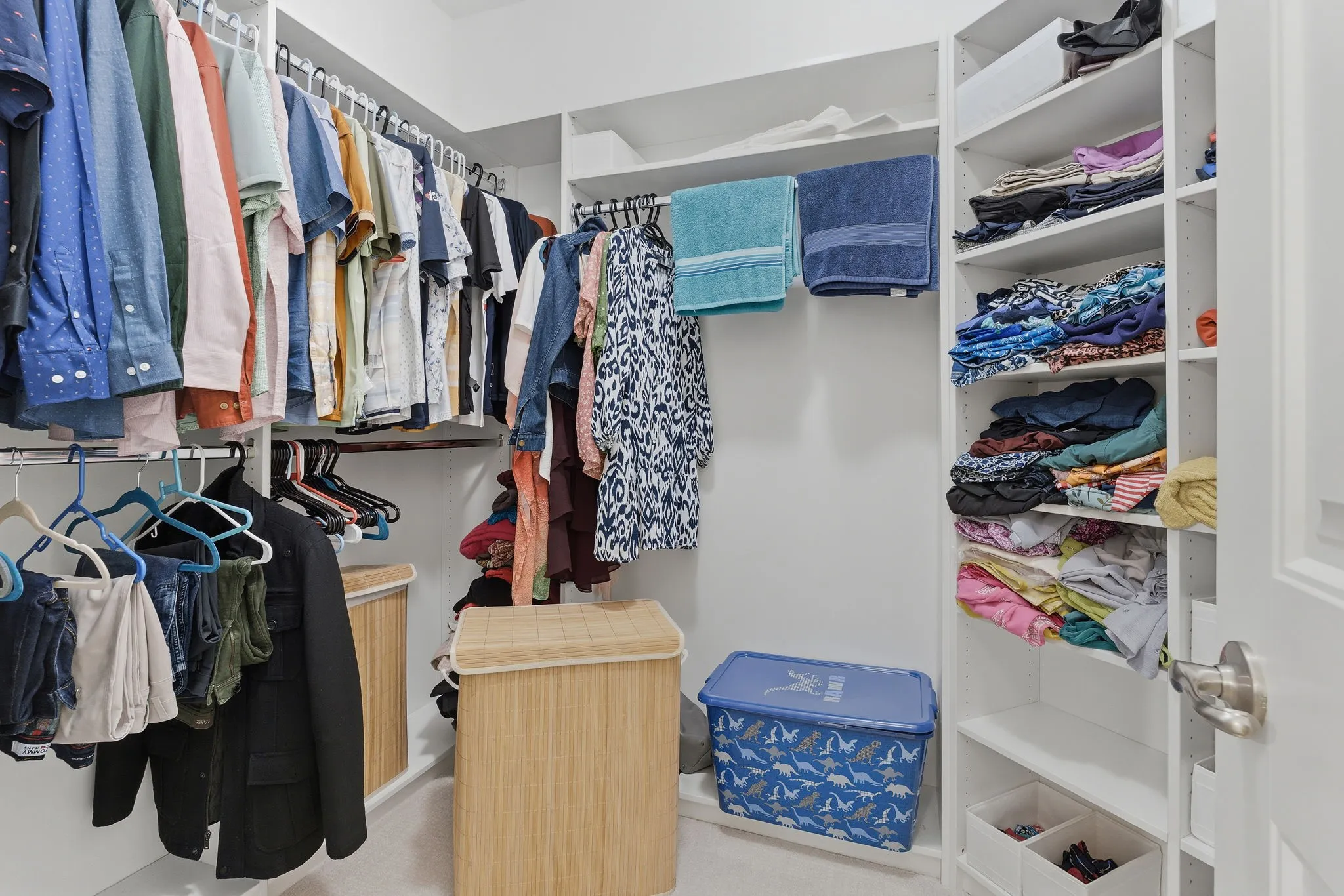 Built-in closet organization system featuring white shelving, multiple hanging rods, and an interior door with a brushed nickel handle
