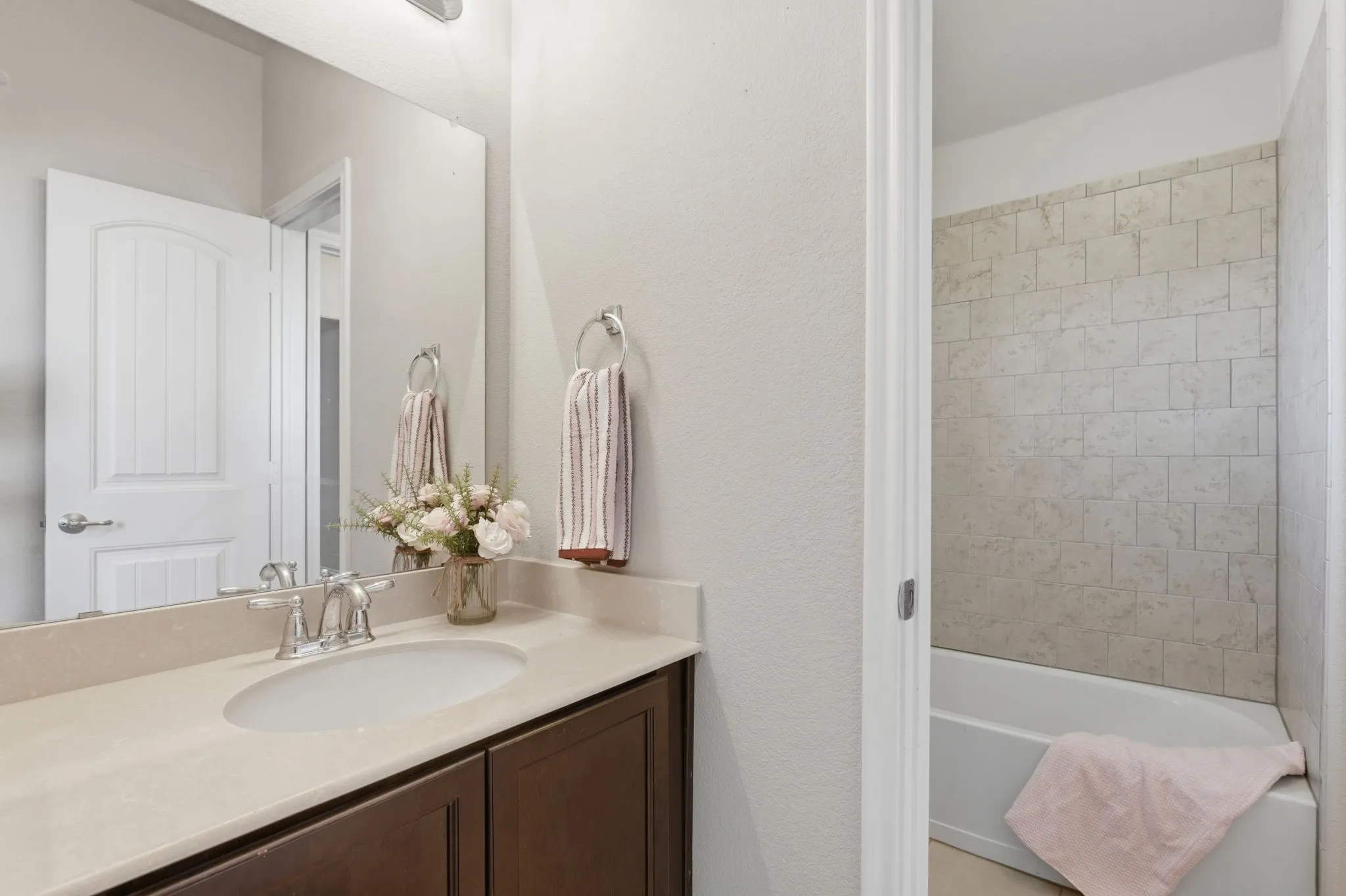 Vanity with a single basin, light-toned countertop, dark wood-finish cabinetry, and a full-width mirror