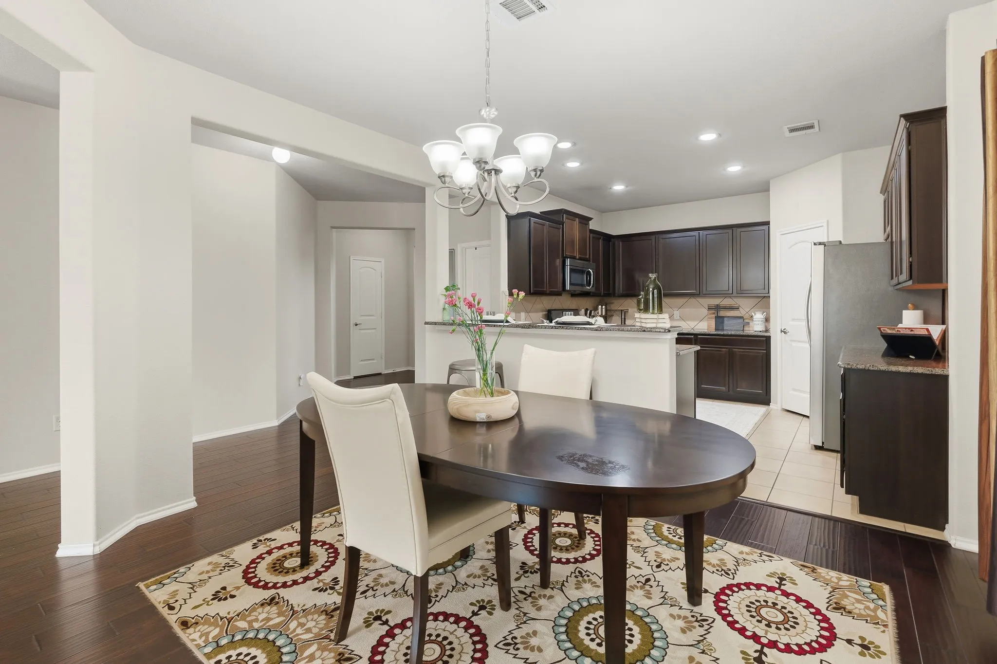 Dark wood-finish flooring throughout, recessed lighting, and a kitchen featuring dark wood cabinetry, stainless steel appliances, and light countertops