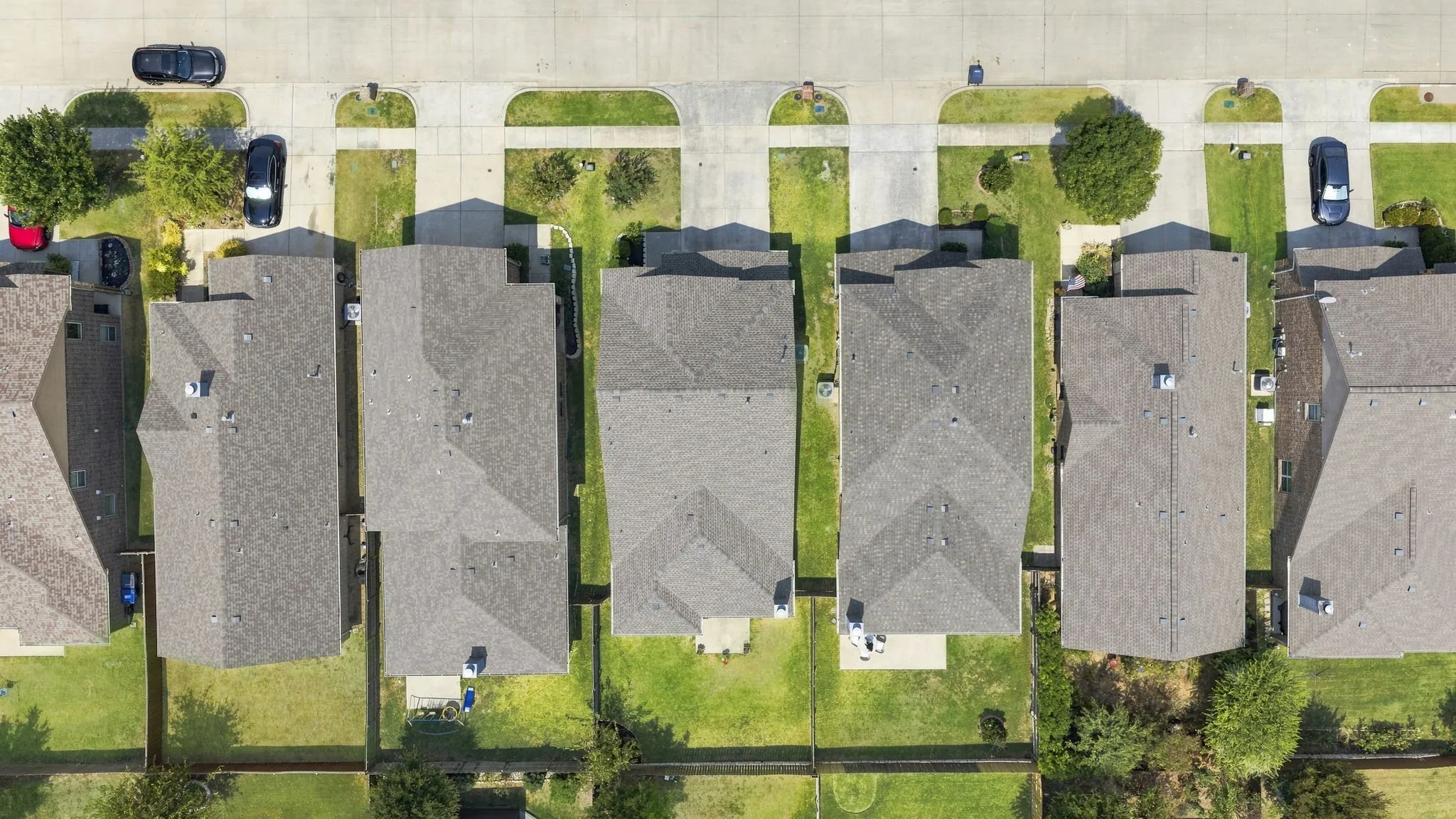 Aerial perspective of residential properties with gray shingle roofs, individual concrete driveways, and manicured front lawns
