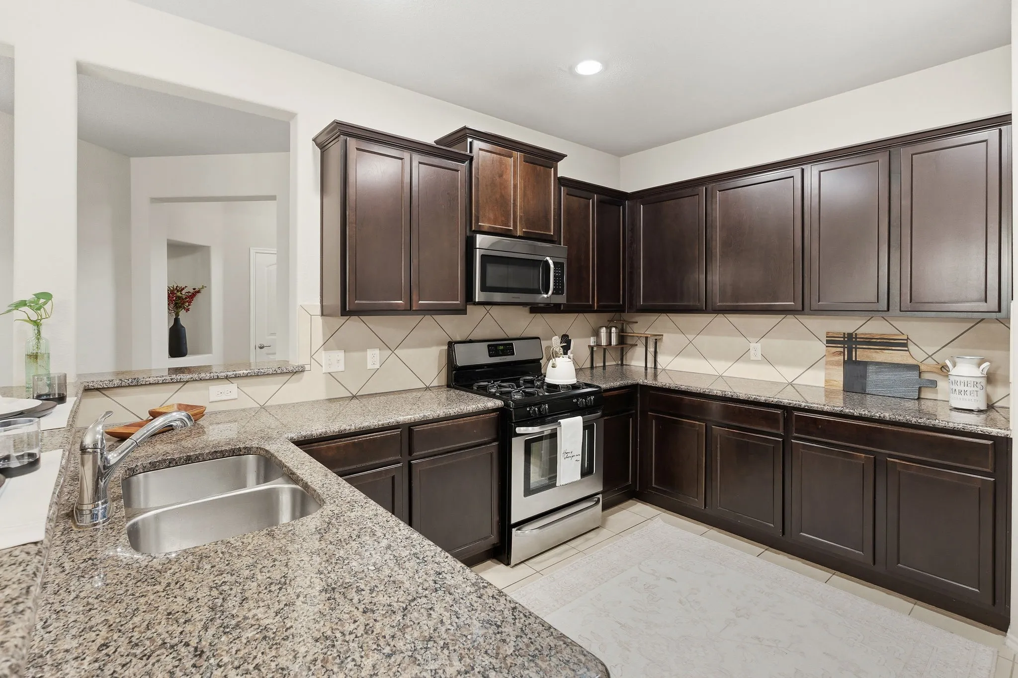 Kitchen featuring dark wood-finish cabinetry, speckled countertops, stainless steel appliances, and a tile backsplash