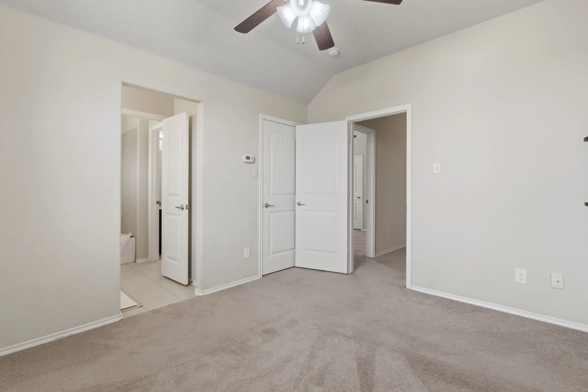 Vaulted ceiling with an attached ceiling fan, neutral wall tones, and carpeted flooring