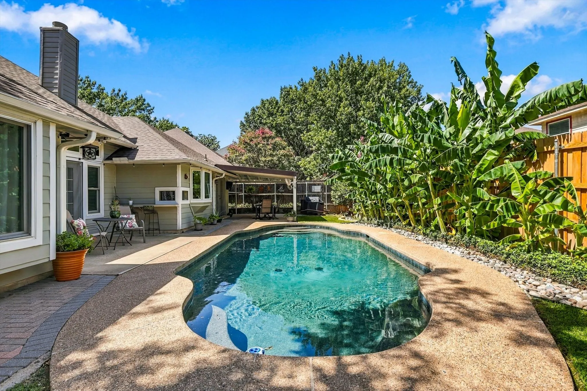 Expansive swimming pool with an exposed aggregate concrete deck and integrated hot tub, complemented by a covered patio with an outdoor bar area