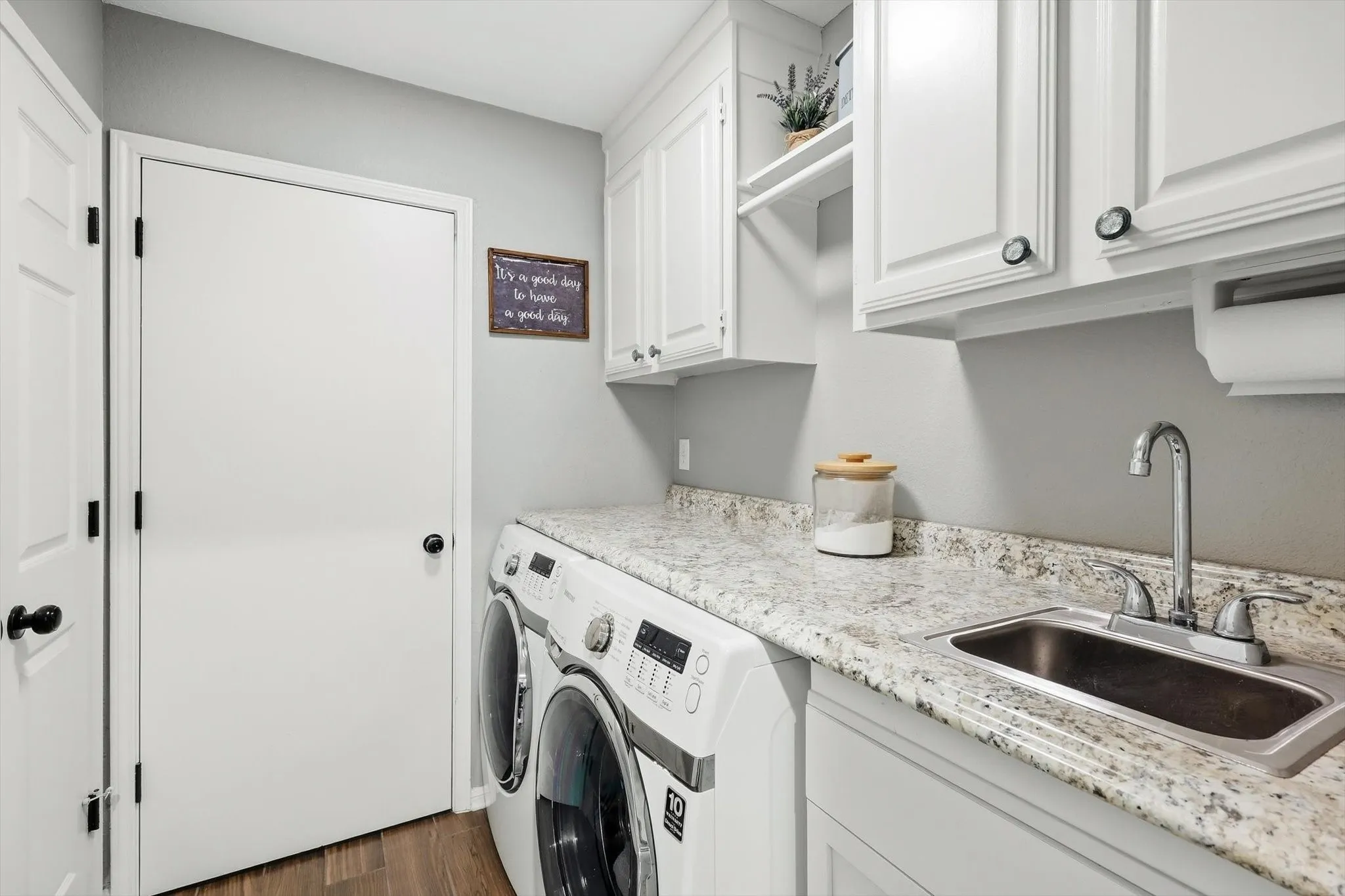 Laundry area featuring wood-finish flooring, white cabinetry, a built-in sink, and a granite-patterned countertop
