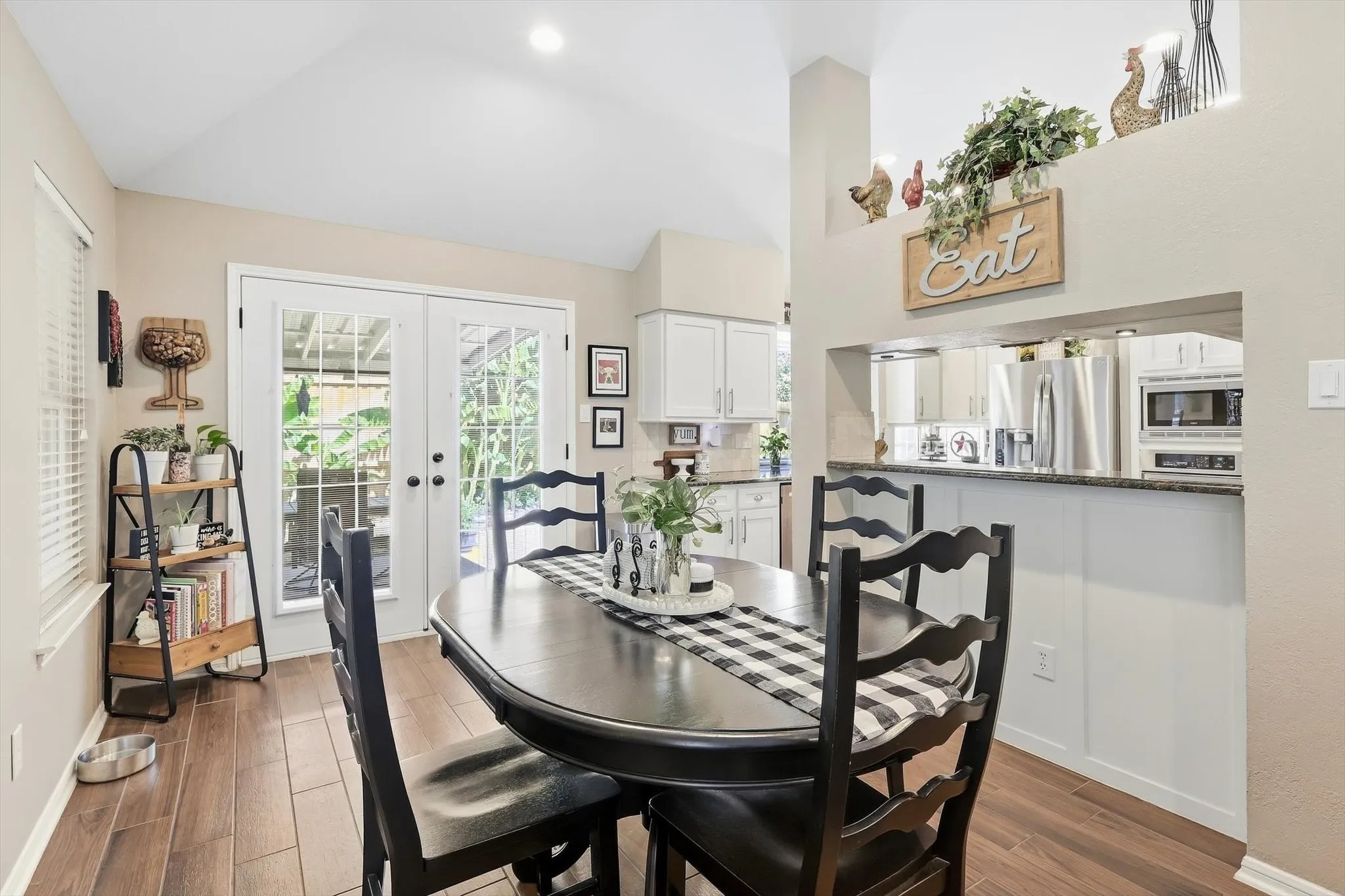 Vaulted ceiling with recessed lighting, wood-finish flooring, white French doors, and a kitchen pass-through with a stone-finish countertop