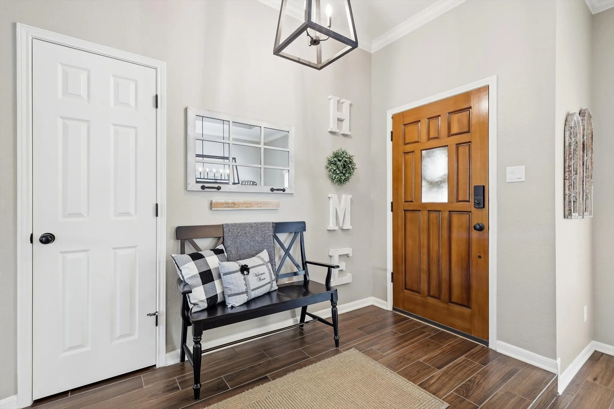 Hardwood-finish flooring, paneled front door with frosted glass insert, white interior door with black hardware, crown molding, and a suspended black metal light fixture