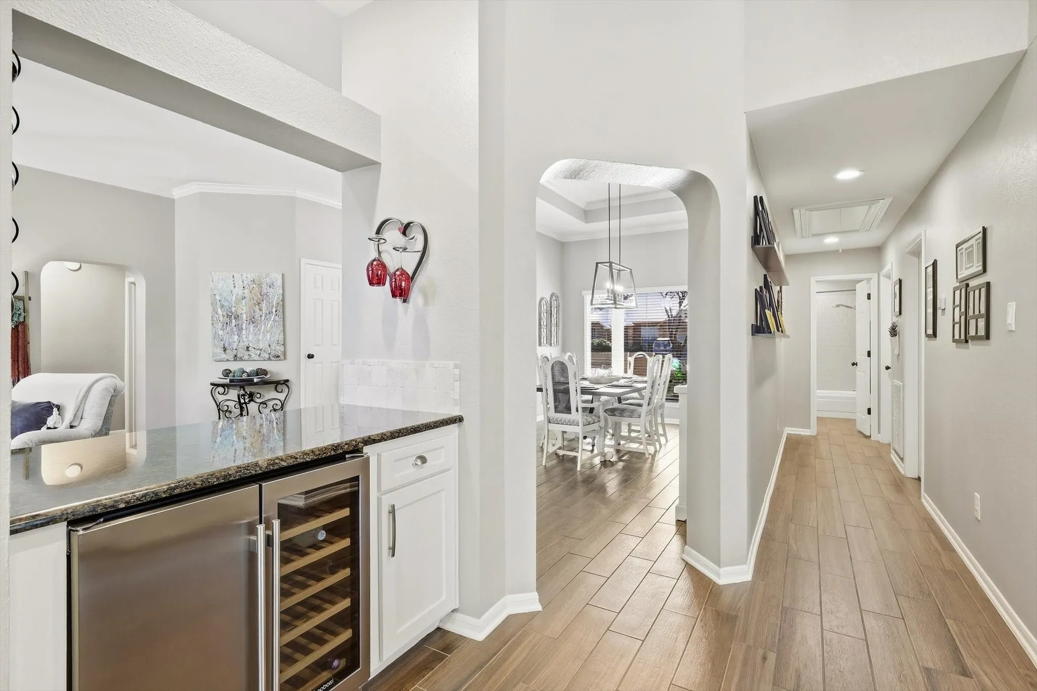 Built-in beverage cooler and wine refrigerator, granite countertop, white cabinetry, wood-finish flooring, and arched entryway