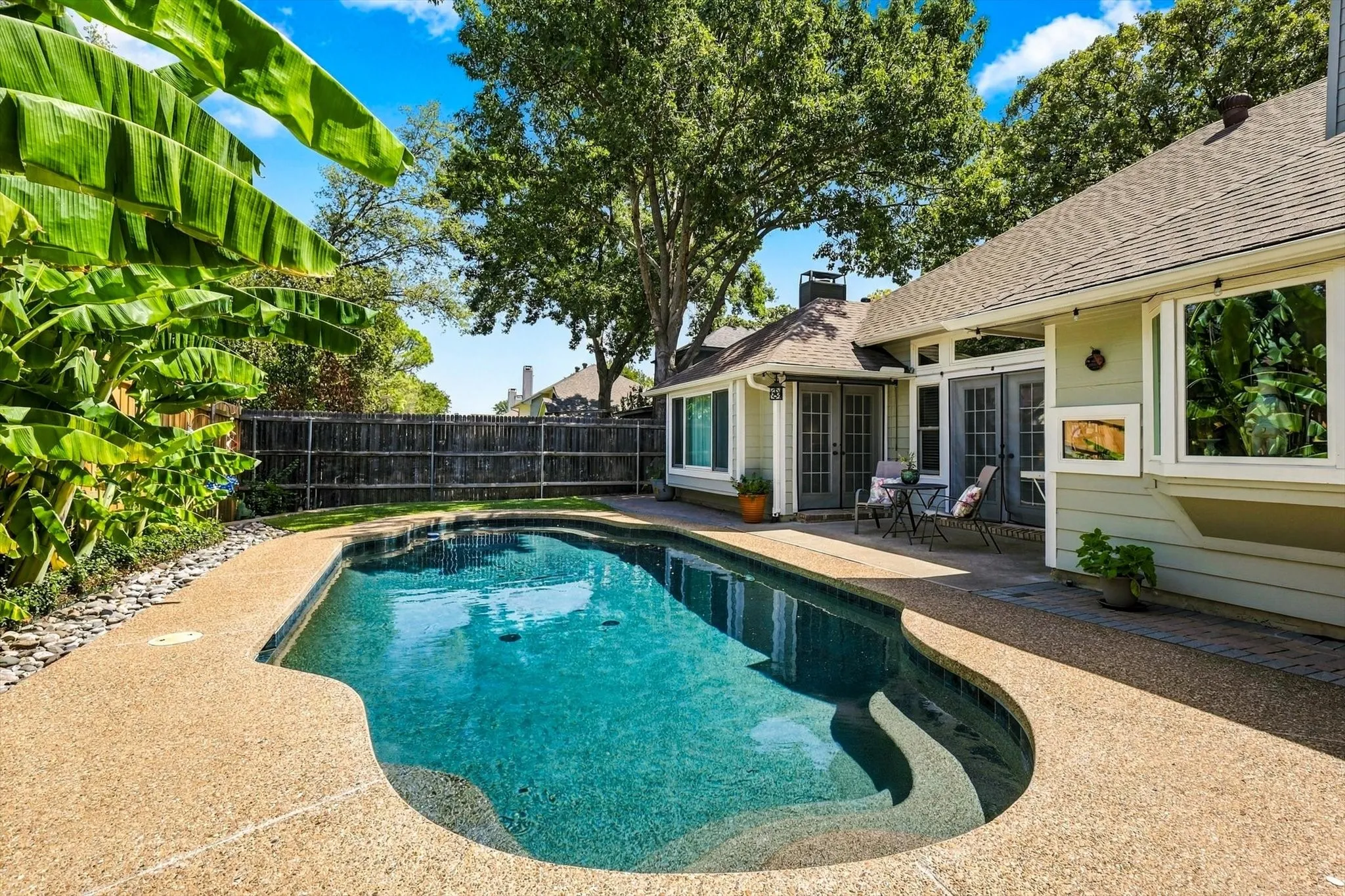 In-ground swimming pool with integrated steps, surrounded by an exposed aggregate concrete patio