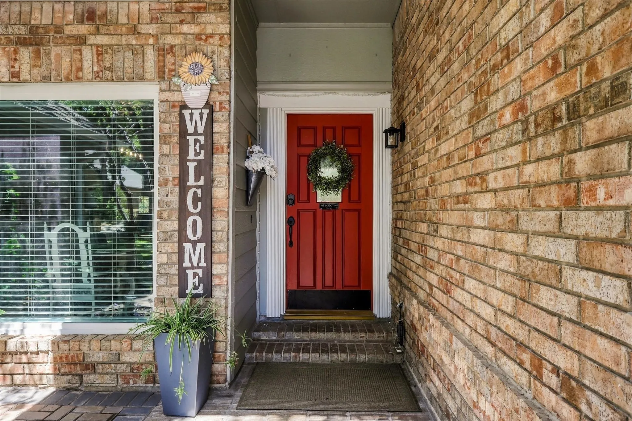 Brick exterior featuring a red entry door with white trim and a black wall-mounted light fixture