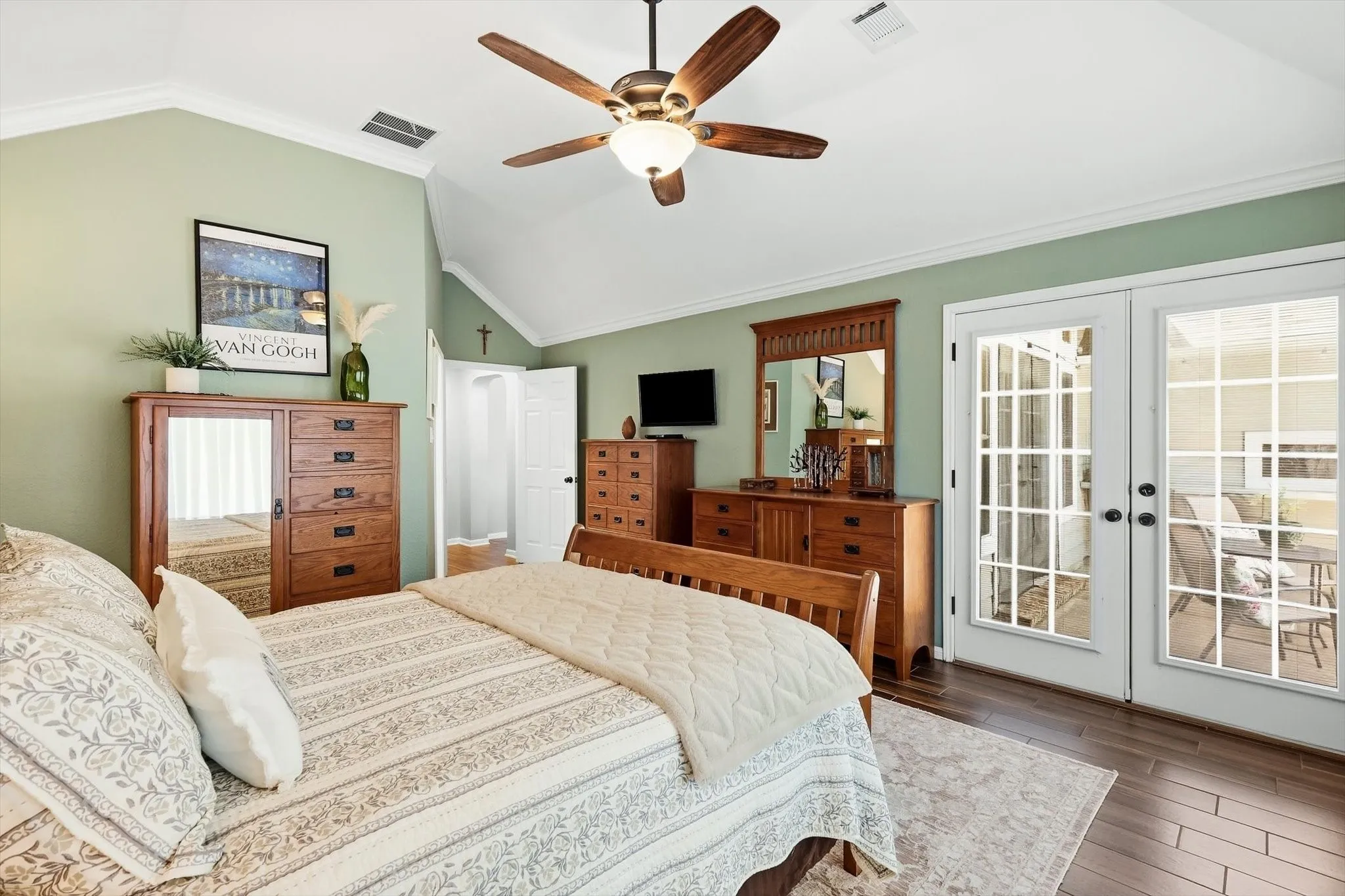 Vaulted ceiling, wood-finish flooring, ceiling fan with integrated lighting, white French doors, and substantial crown molding