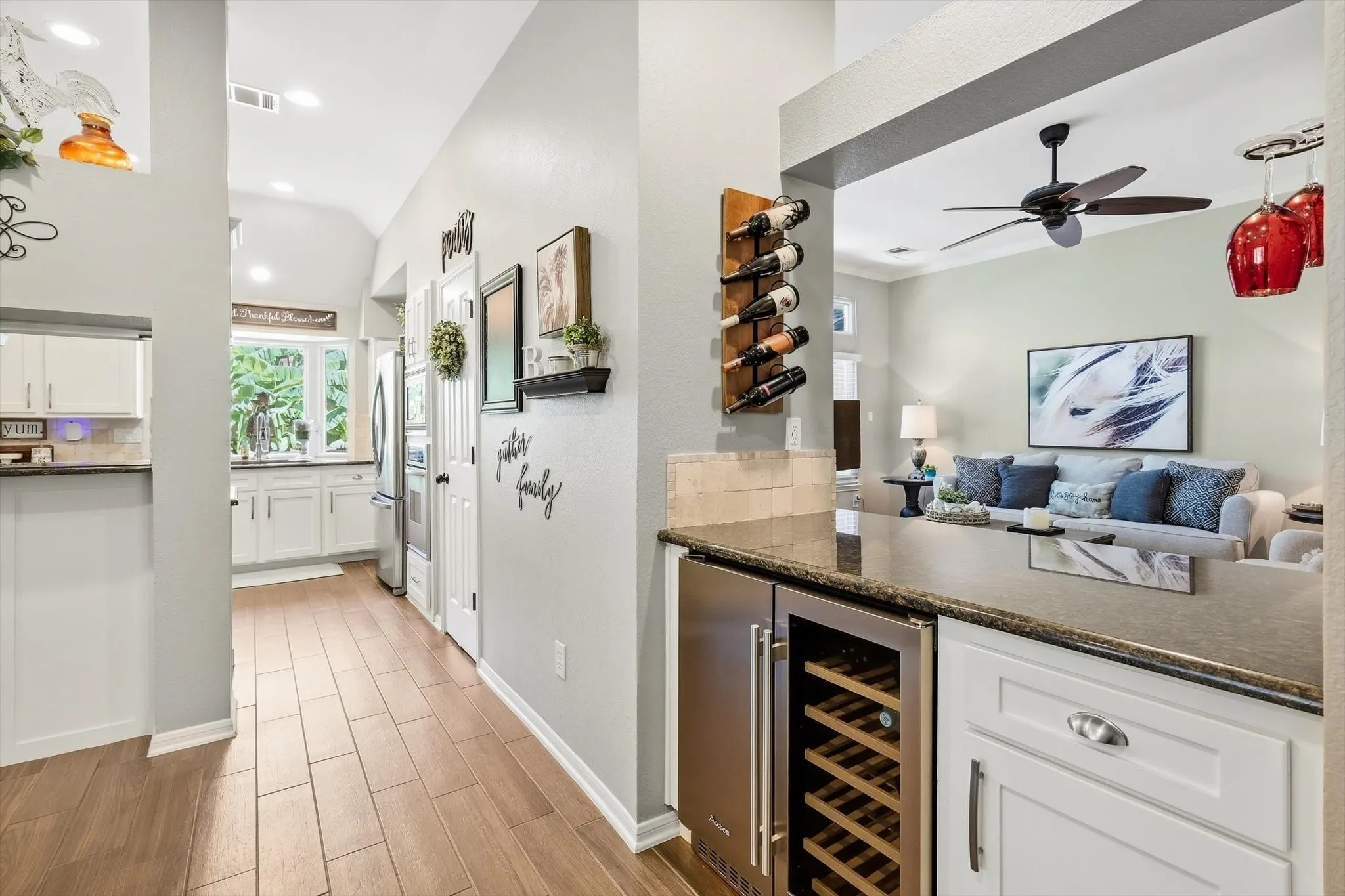 Built-in wine refrigerator, granite-style countertops, wood-finish flooring, white cabinetry, and stainless steel appliances