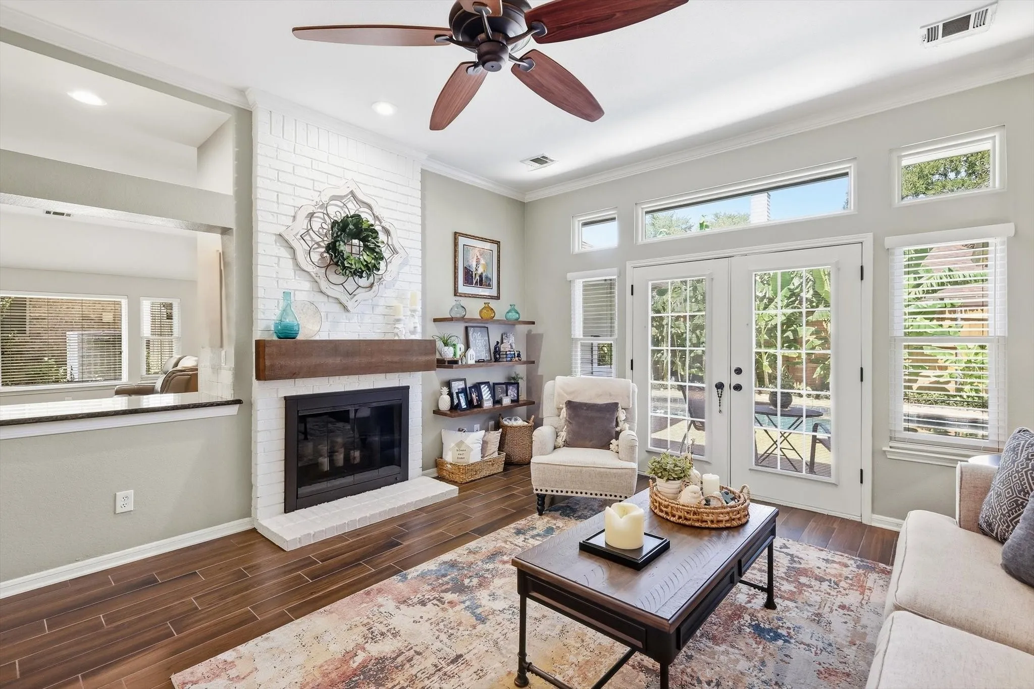Living area featuring wood-finish flooring, a white brick fireplace with a wood mantle, and a ceiling fan