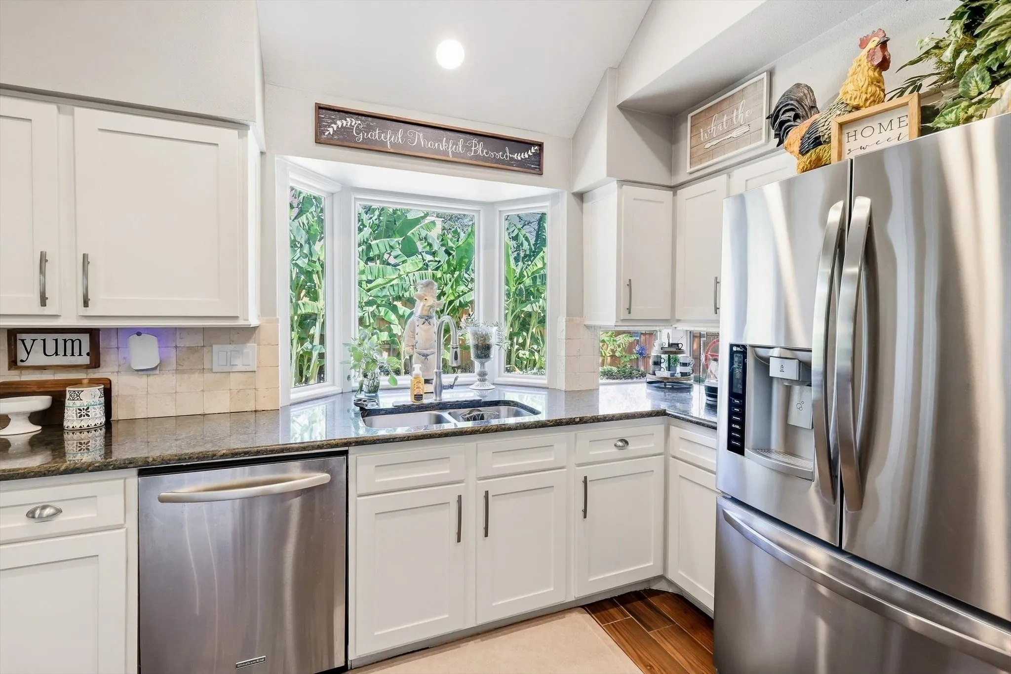 White shaker-style cabinetry, stainless steel appliances, bay window, granite countertops, and wood-finish flooring