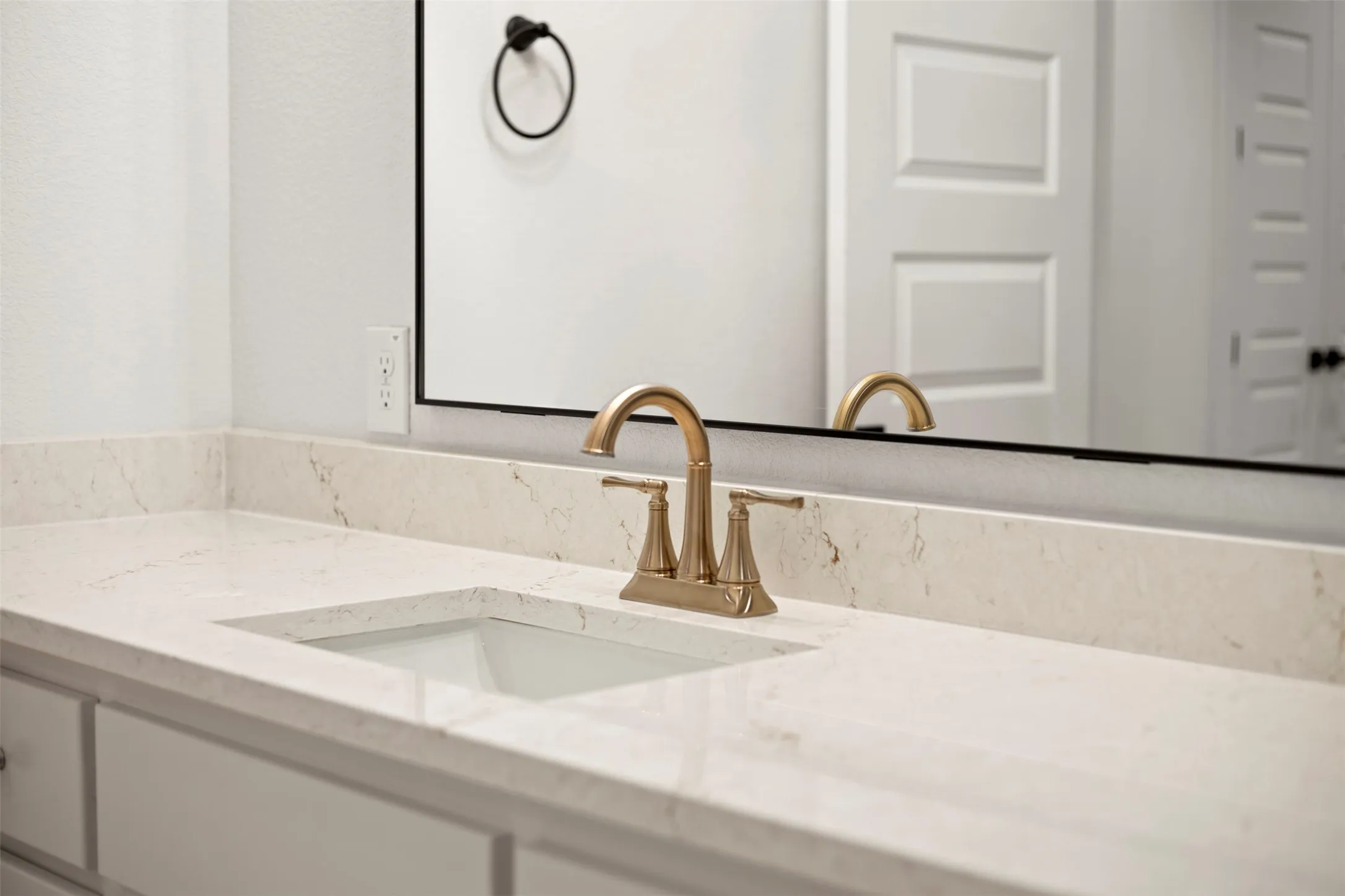 Integrated sink with brass-finish faucet, light-toned countertop, and white cabinetry
