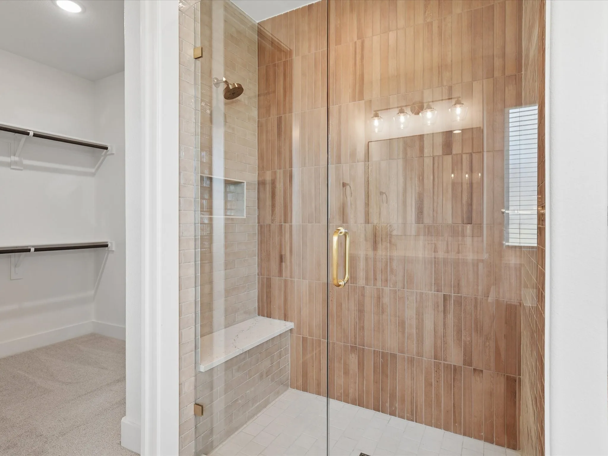 Glass-enclosed shower with wood-look tile surround, built-in bench, recessed niche, and gold-finish fixtures