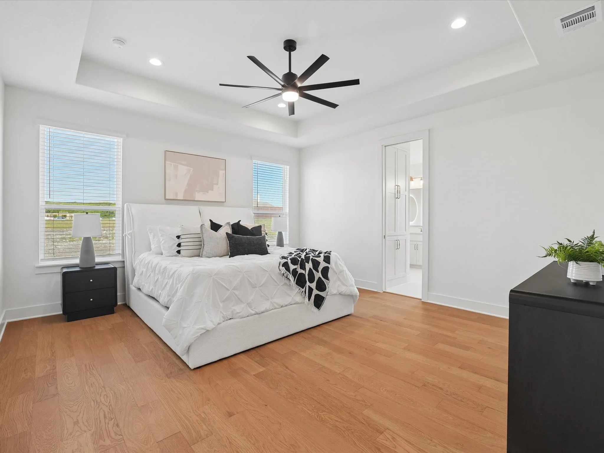Tray ceiling with recessed lighting, wood-finish flooring, ceiling fan, and dual windows