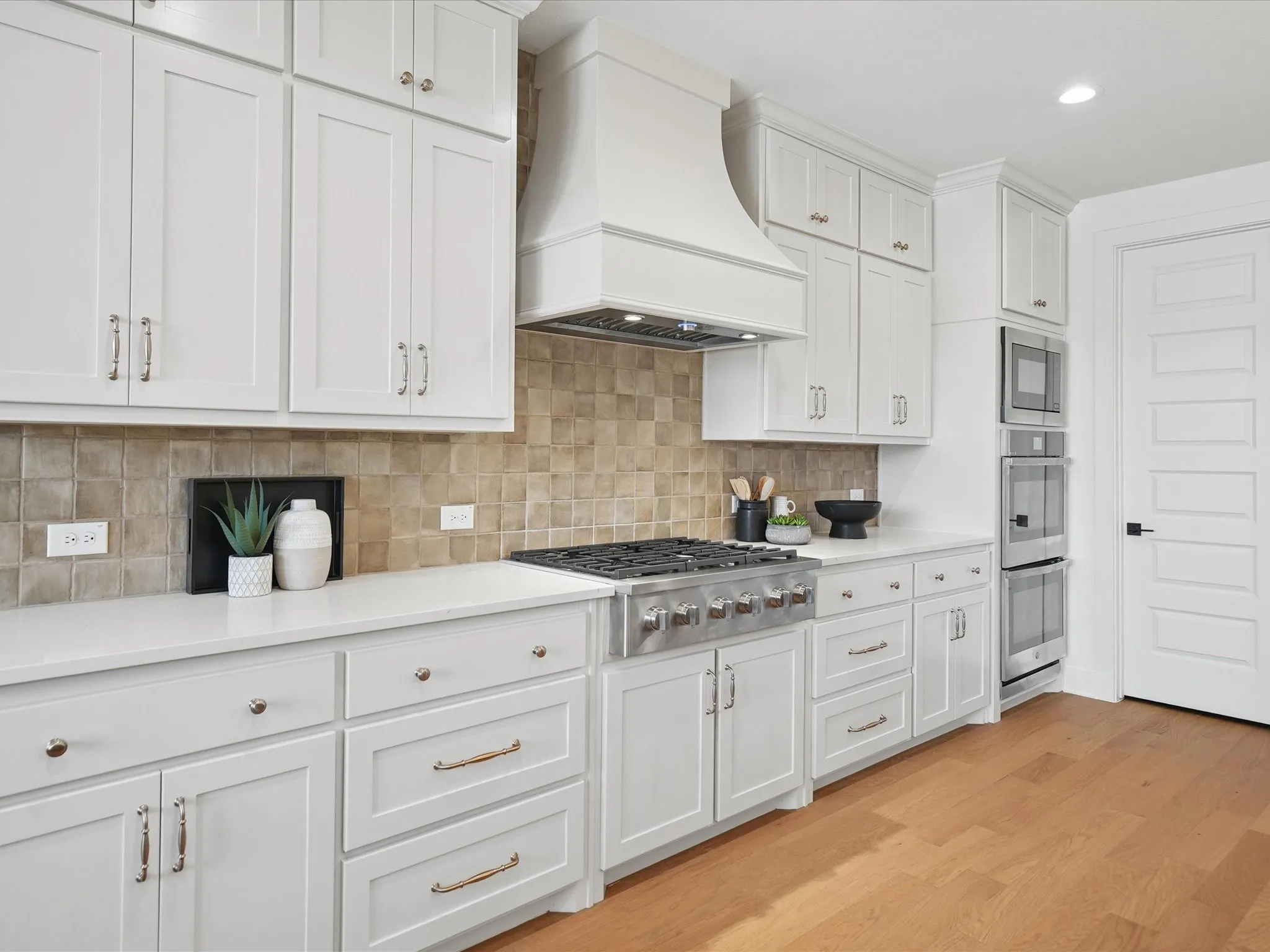Kitchen featuring white shaker cabinetry, light-toned tiled backsplash, white countertops, built-in stainless steel appliances, and wood-finish flooring