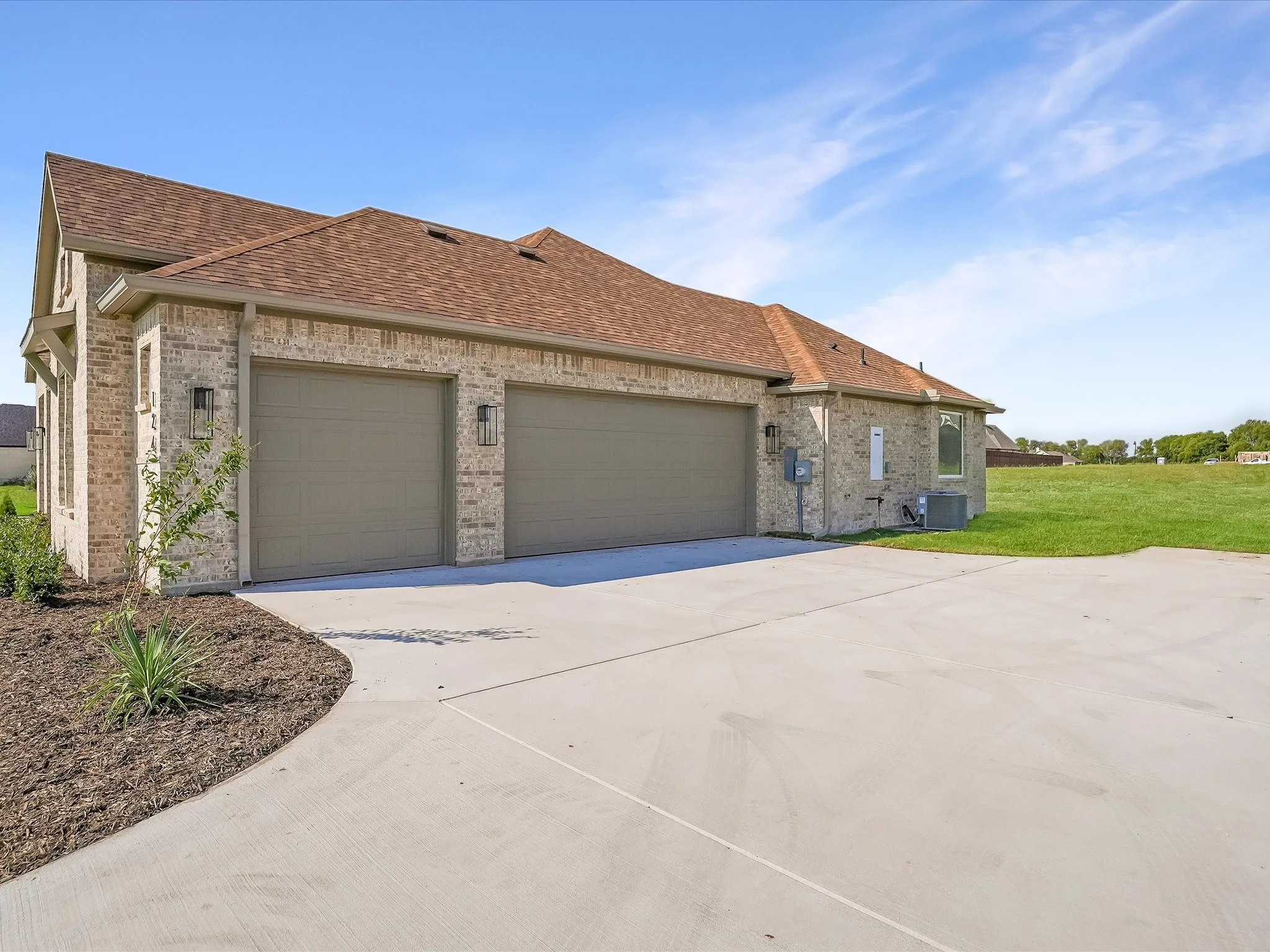 Brick exterior with a peaked roofline, two-car garage doors, attached exterior lighting, and a paved driveway