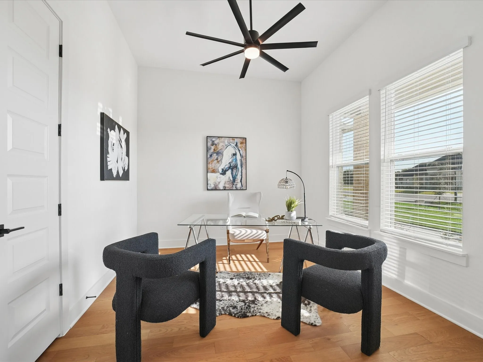 Hardwood flooring, white paneled door with black hardware, two large windows, vaulted ceiling, and a modern ceiling fan with integrated lighting